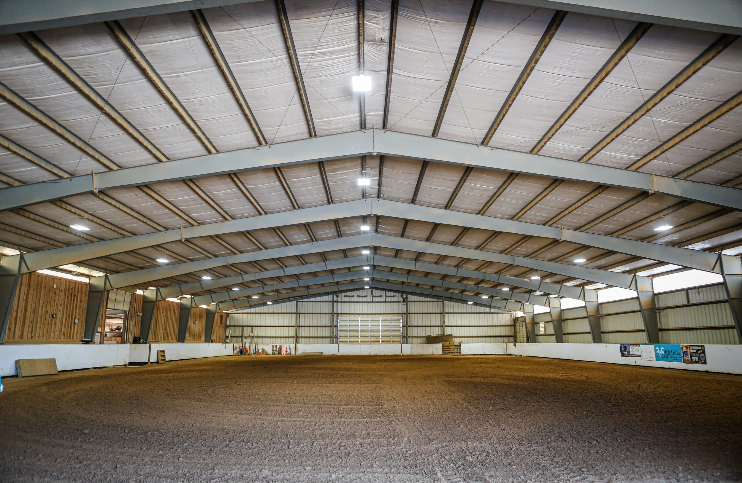 Indoor equestrian arena with dirt ground and metal roof structure