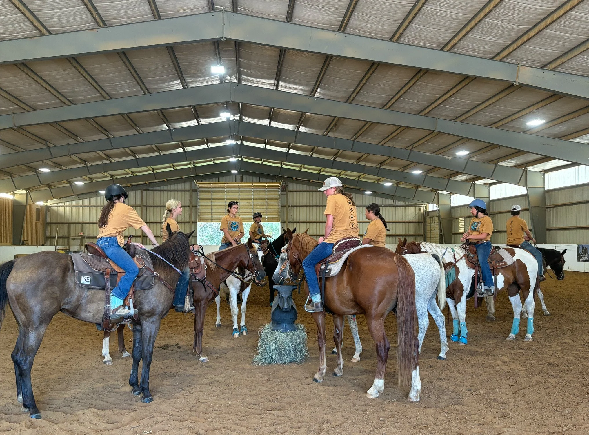 Group of people riding horses inside an indoor riding arena.