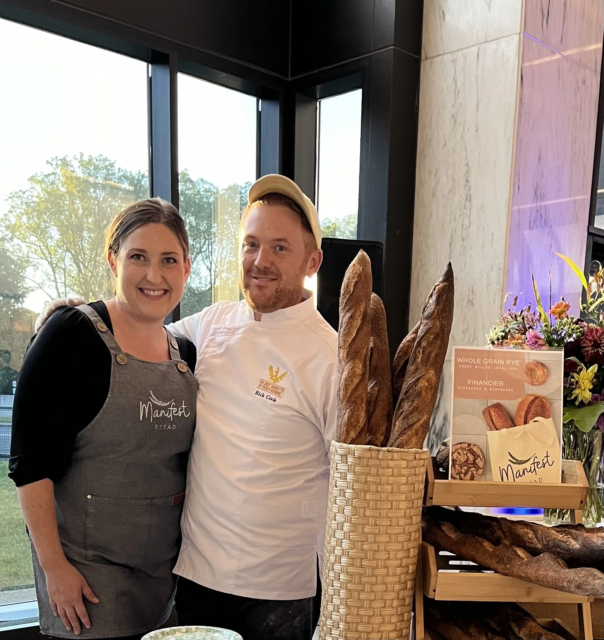 Rick and Tyes cook pictured in Aprons in front of baguette display