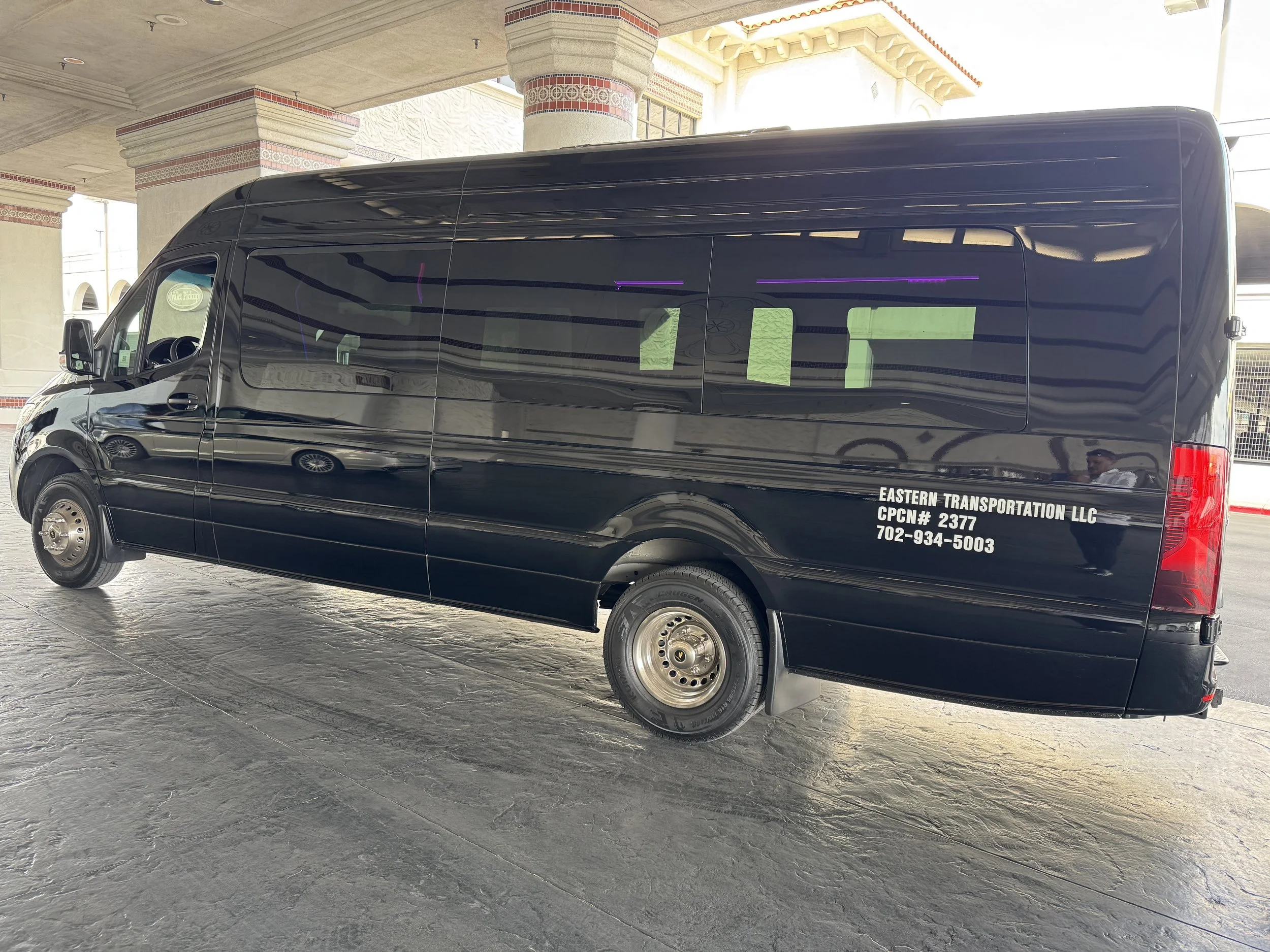 Black passenger shuttle van labeled Eastern Transportation LLC parked beneath a hotel porte-cochère.
