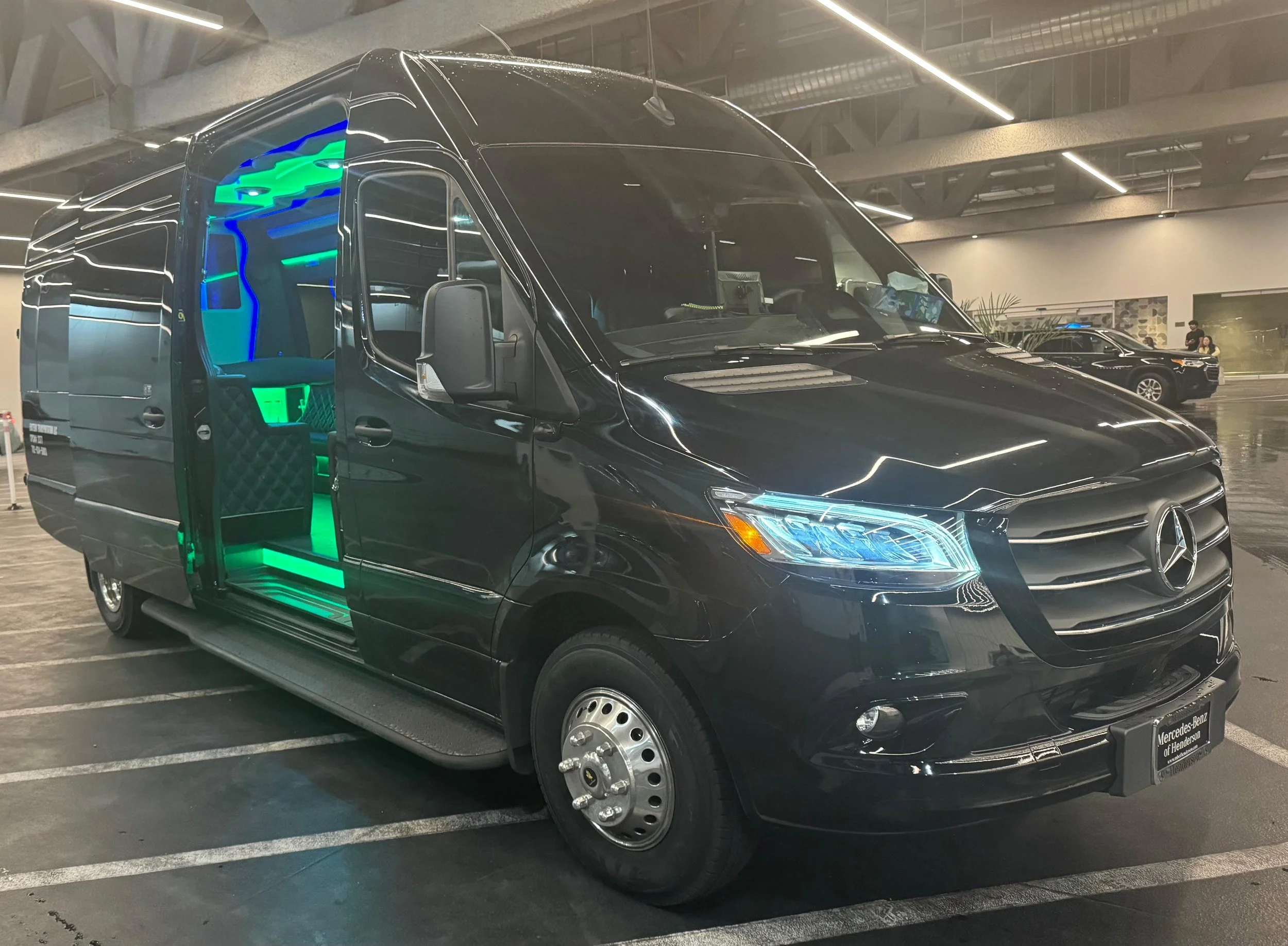 Black Mercedes-Benz luxury passenger van with an open sliding door and green interior lighting in an indoor showroom