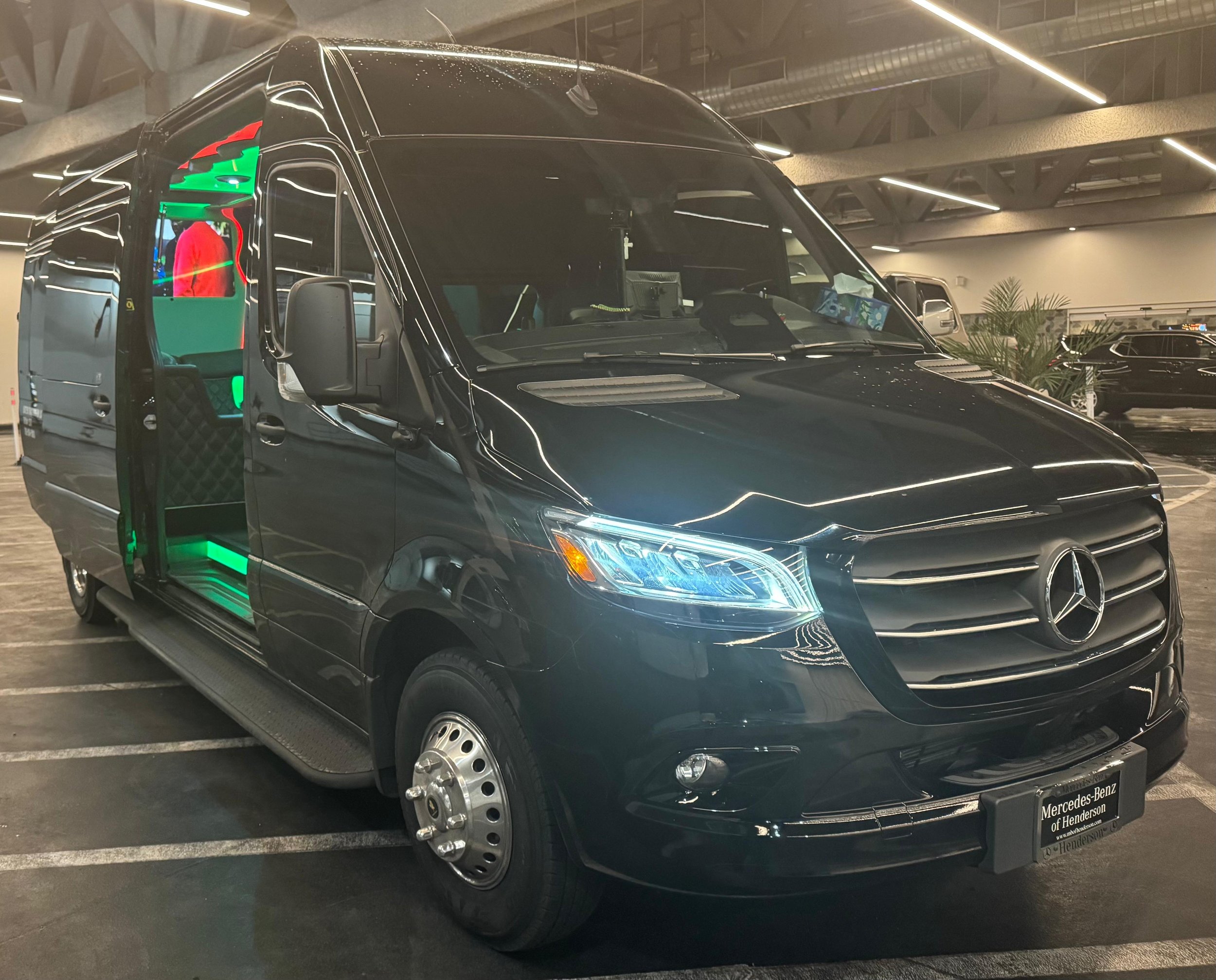 Black Mercedes-Benz Sprinter luxury van with open sliding door and green interior lighting in an indoor showroom