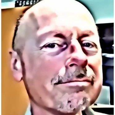 Close-up of a middle-aged man with a bald head, mustache, and beard, making a slightly amused or skeptical facial expression.