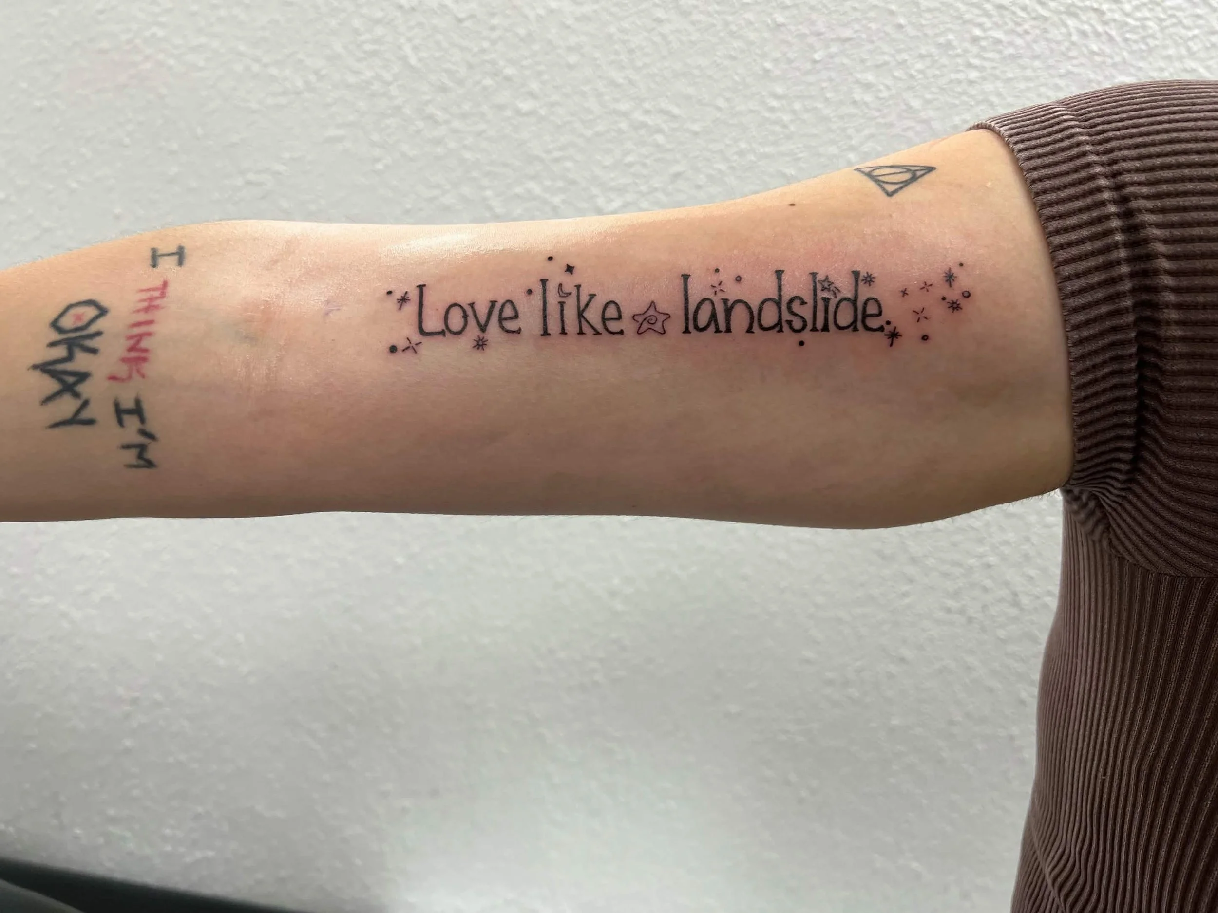 A person with a tattoos on their arm that reads 'Love like landscape' surrounded by small stars and dots.