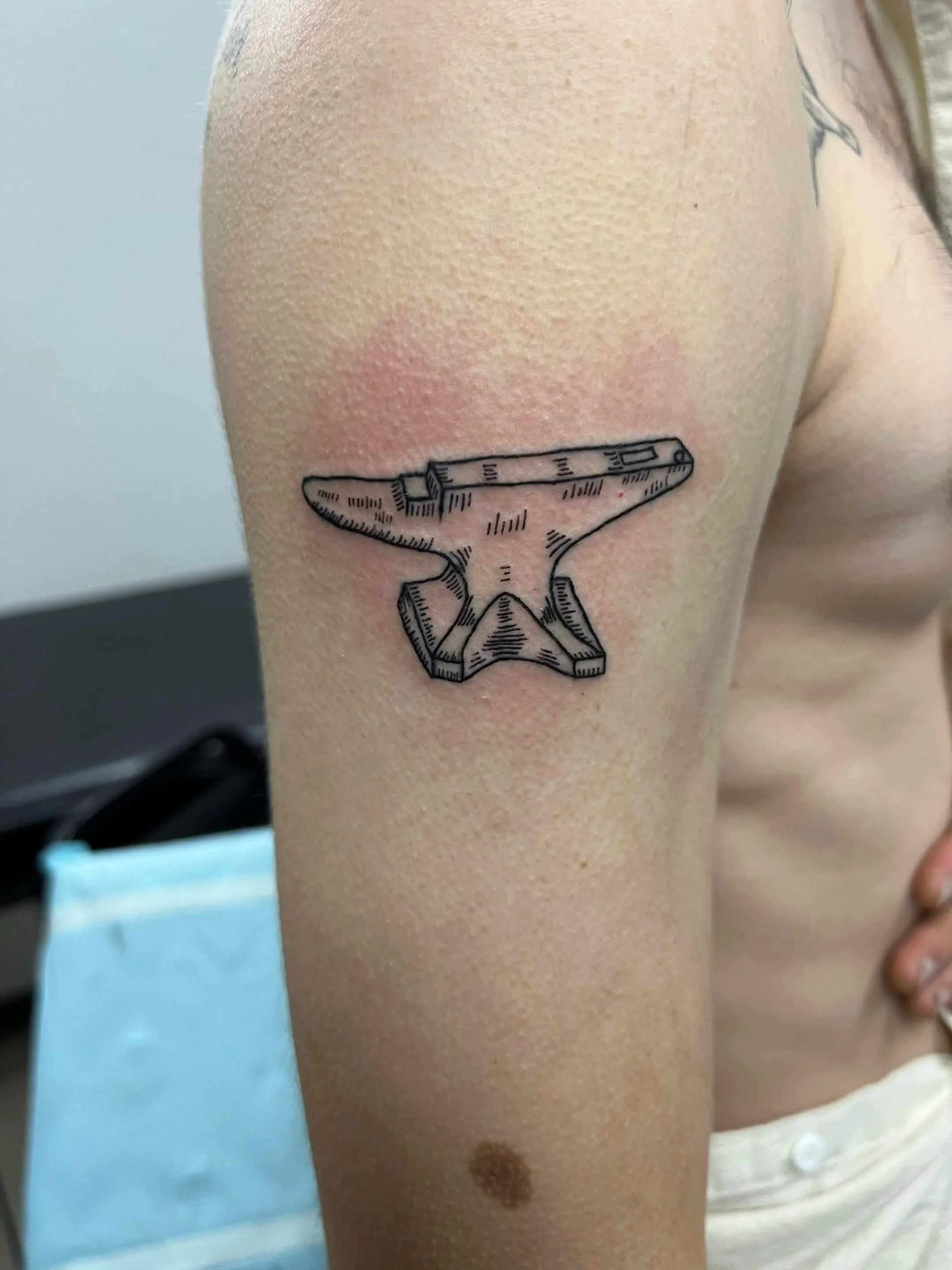 Close-up of a person's arm with a black outline tattoo of a microscope on the upper arm.