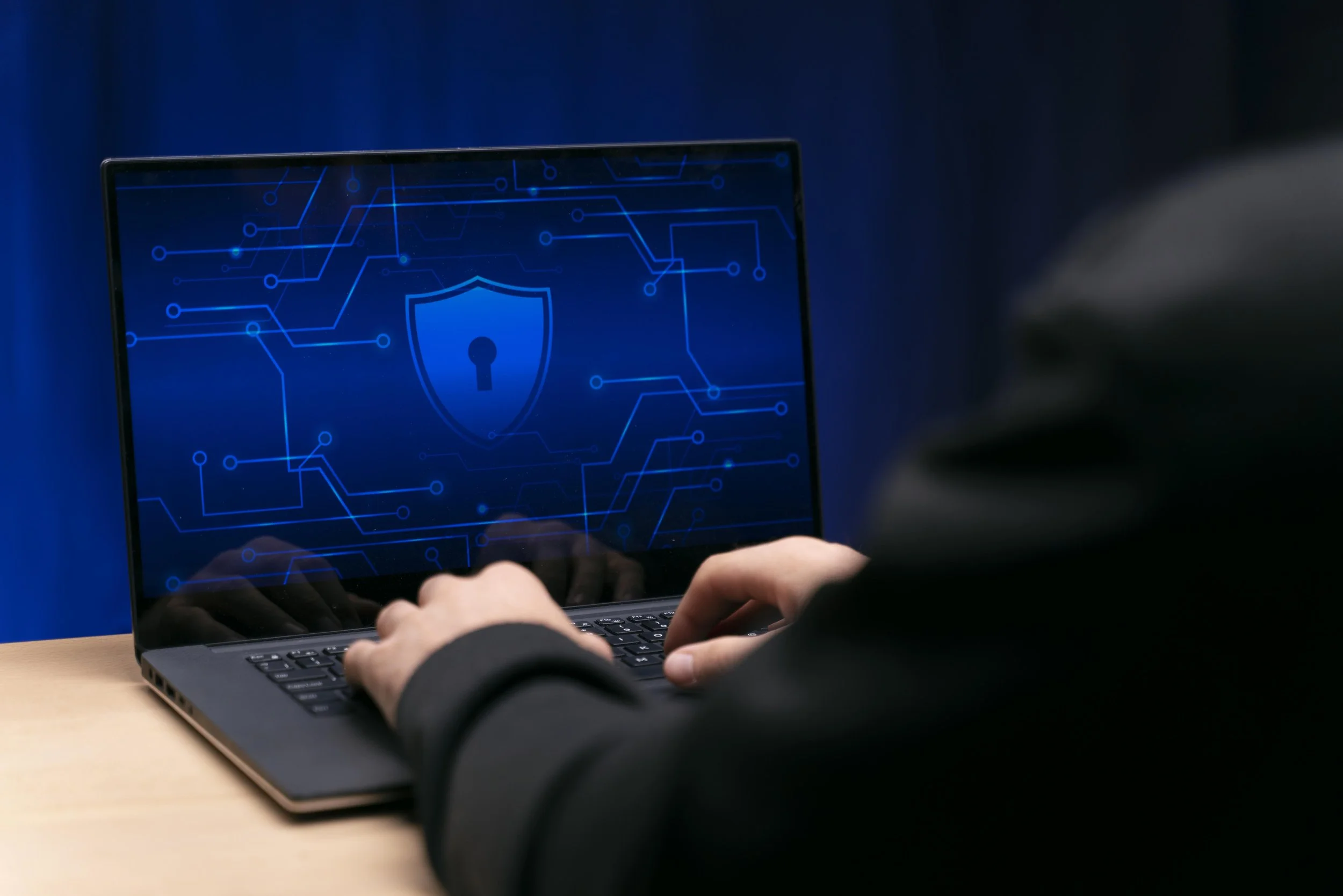A person working on a laptop with a digital security shield graphic on the screen