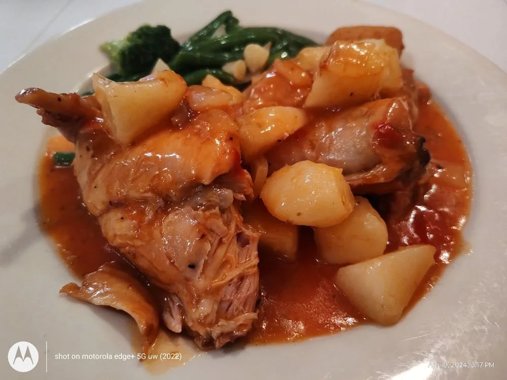 Plate of chicken with potatoes, garlic greens, and broccoli in a sauce.