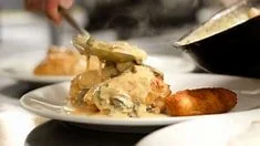 Close-up of a serving of creamy casserole with a fork lifting a scoop, accompanied by a biscuit, on a white plate.
