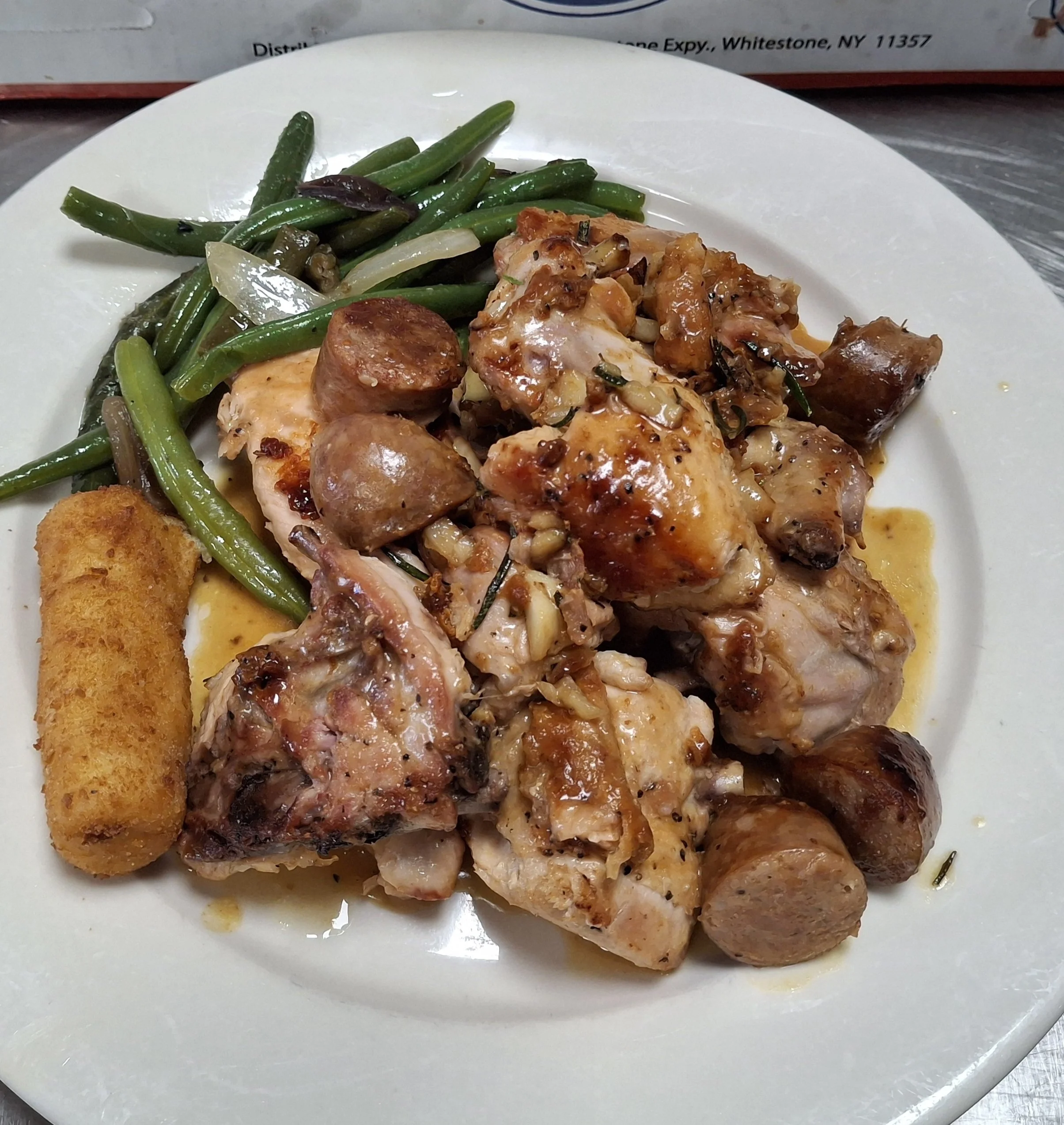 Plate of cooked chicken with sausage, mushrooms, and vegetables, including green beans and onions.