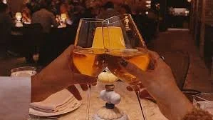 Two people clinking glasses of wine in a restaurant setting at night.