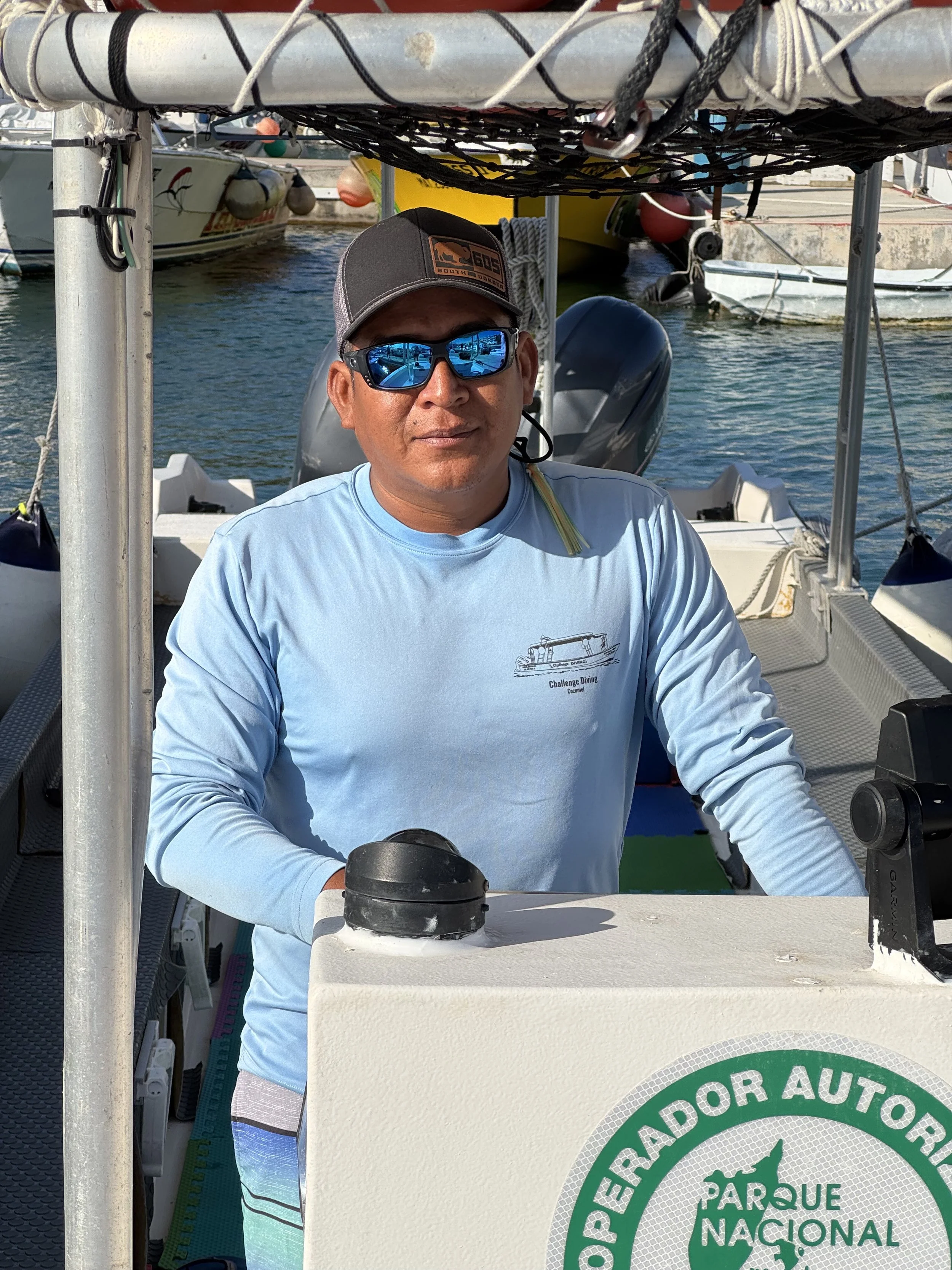 Challenge Diving Baby Shark Captain, Charlie, in a light blue long-sleeve shirt, wearing sunglasses and a baseball cap, operating a boat at the marina.