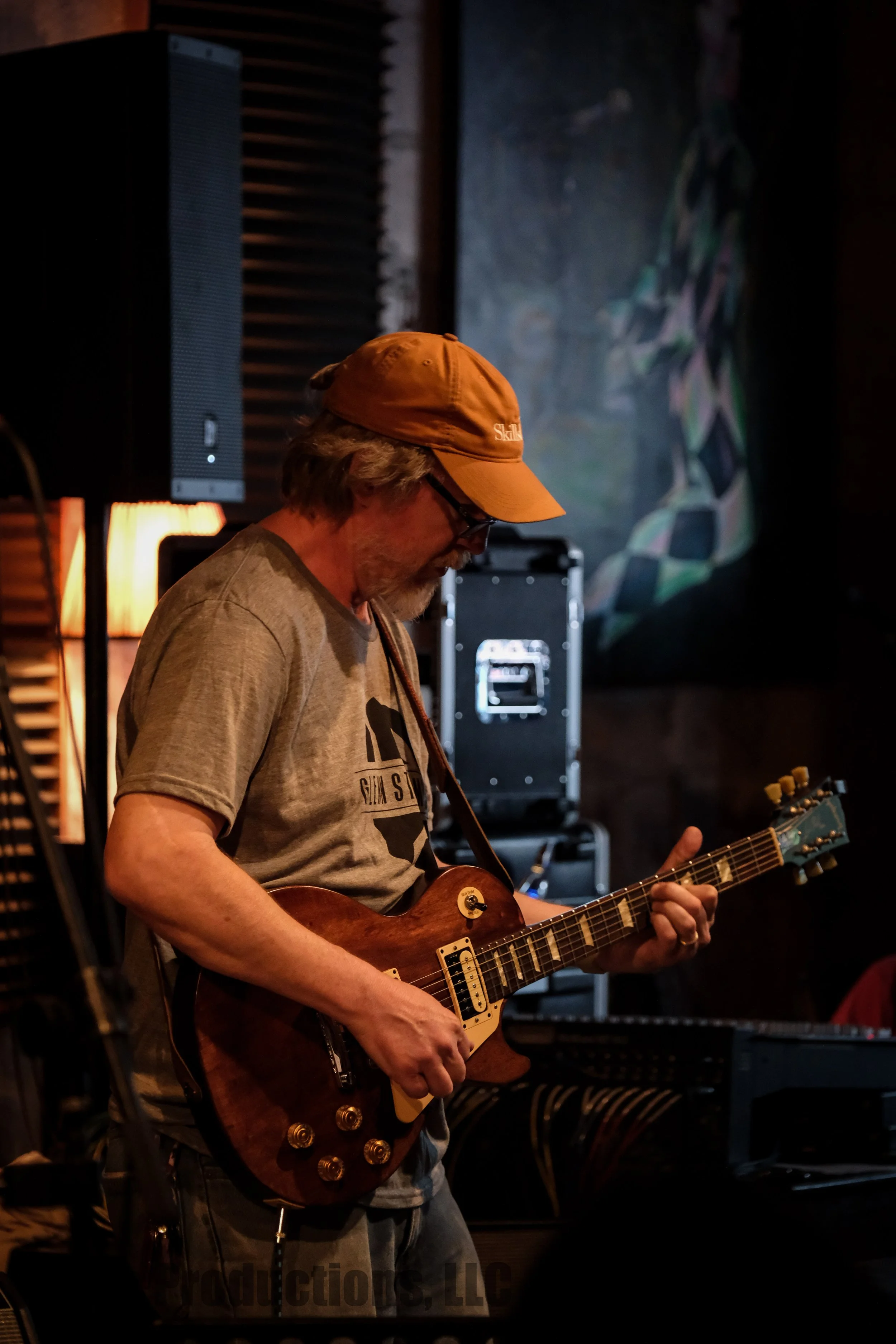 Musician wearing an orange baseball cap playing a brown electric guitar onstage.