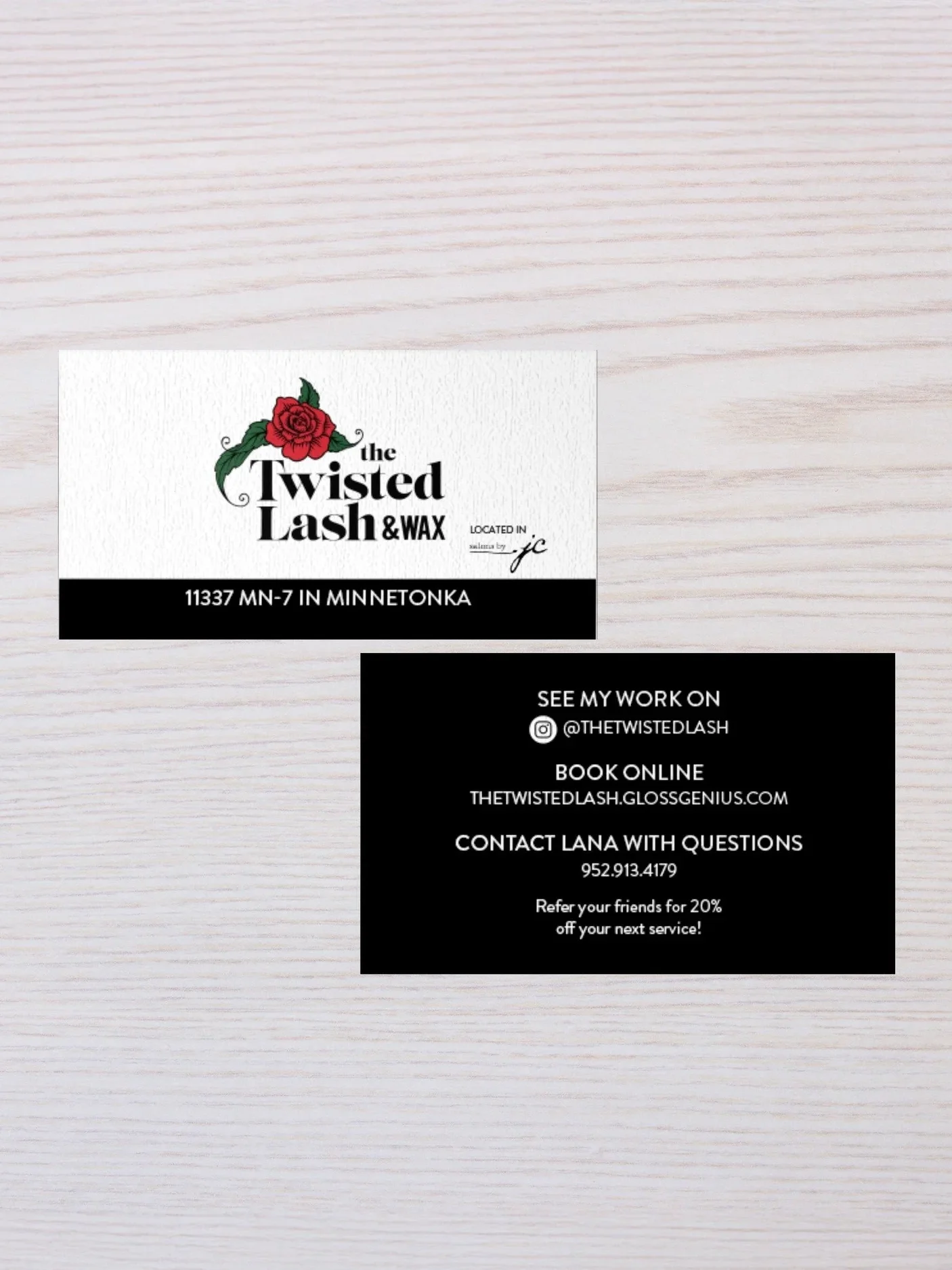 Business card for The Twisted Lash & Wax with a red rose illustration and contact information, laid on a white wooden surface.