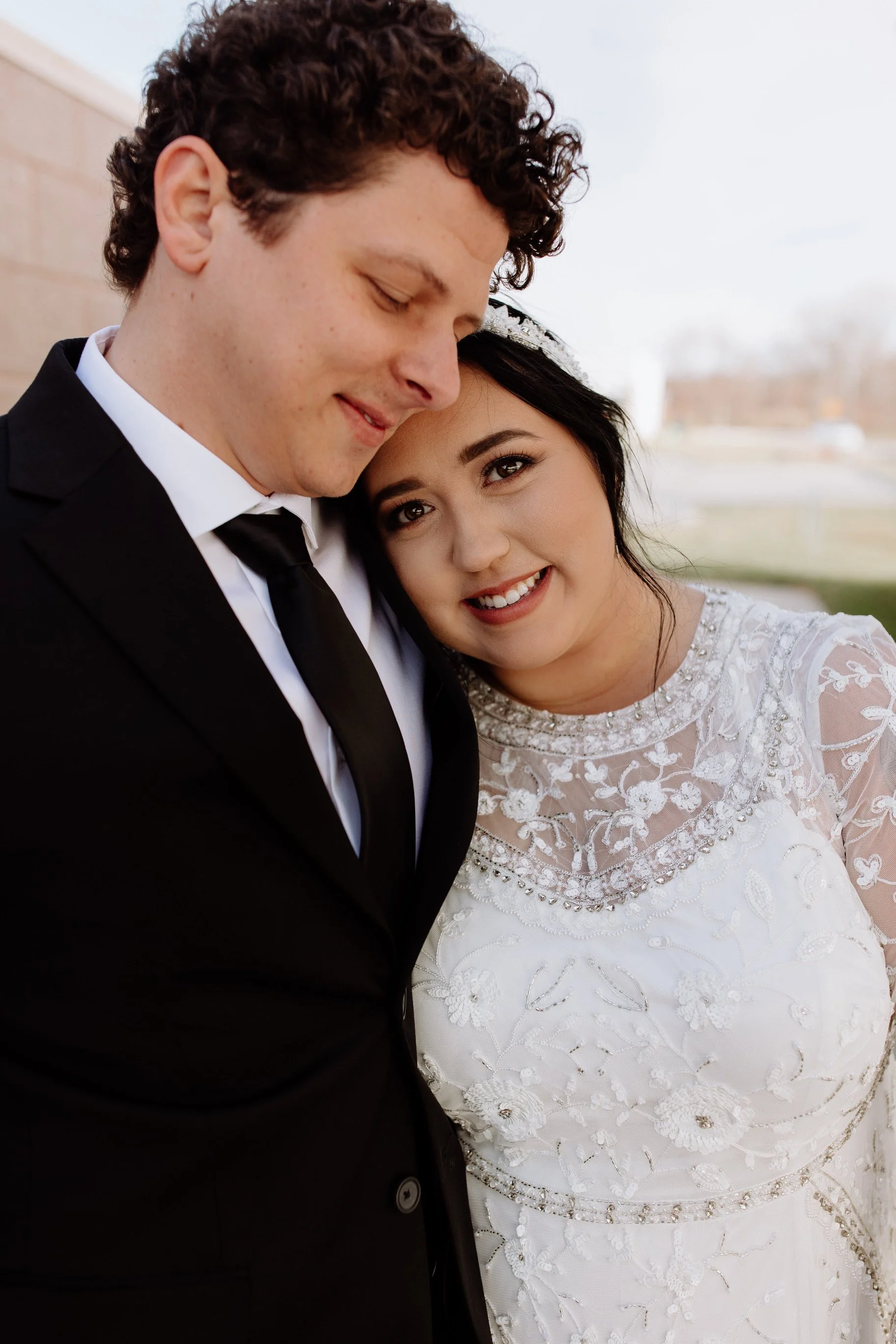 Close-up of a happy bride and groom on their wedding day, with the bride smiling and resting her head on the groom's shoulder.