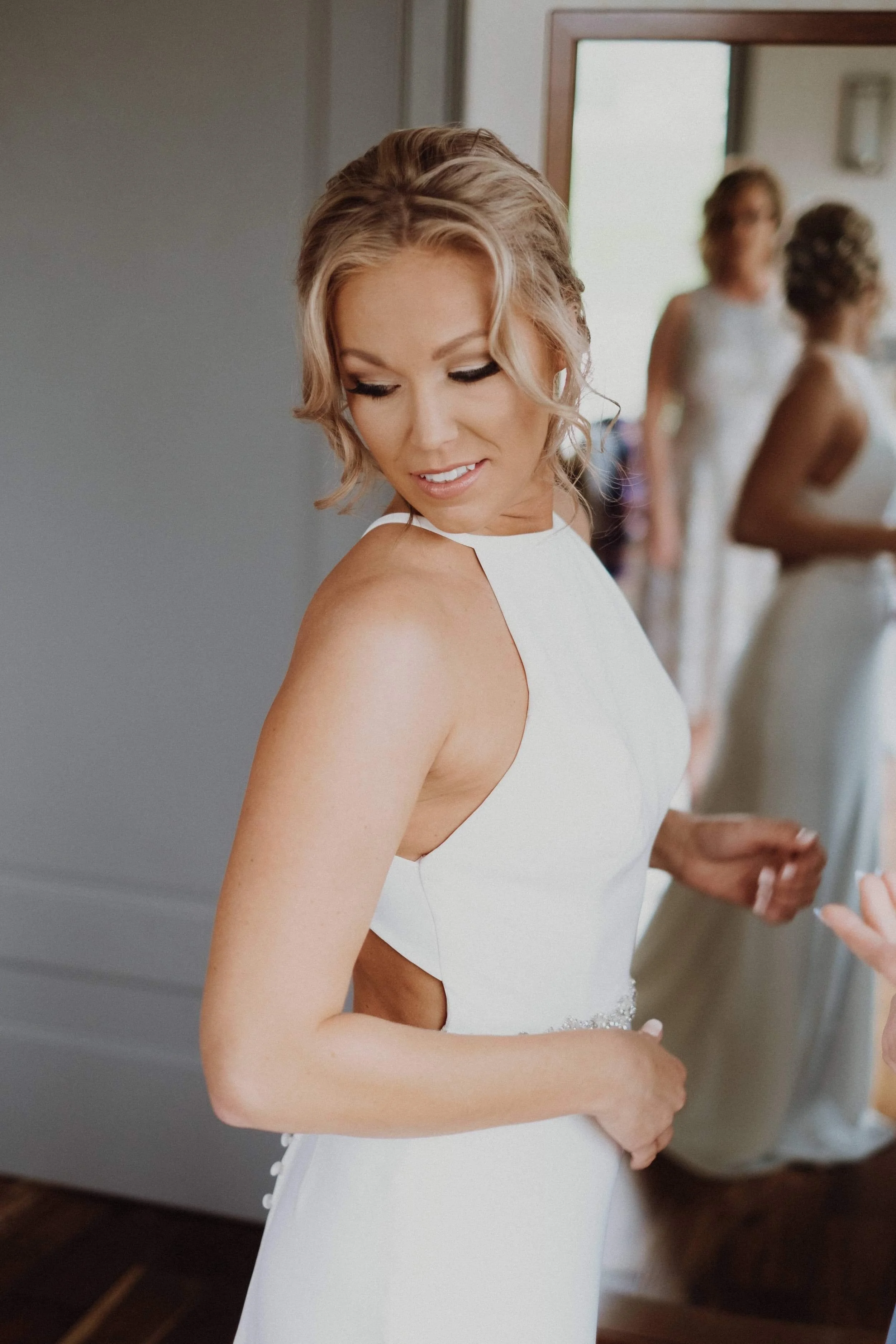 Bride in a white dress getting ready, with bridesmaids in the background.