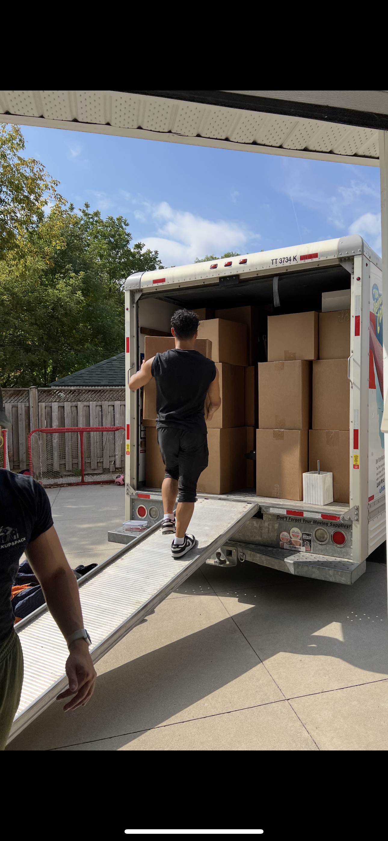 Person loading boxes into a moving truck with a ramp in a backyard.