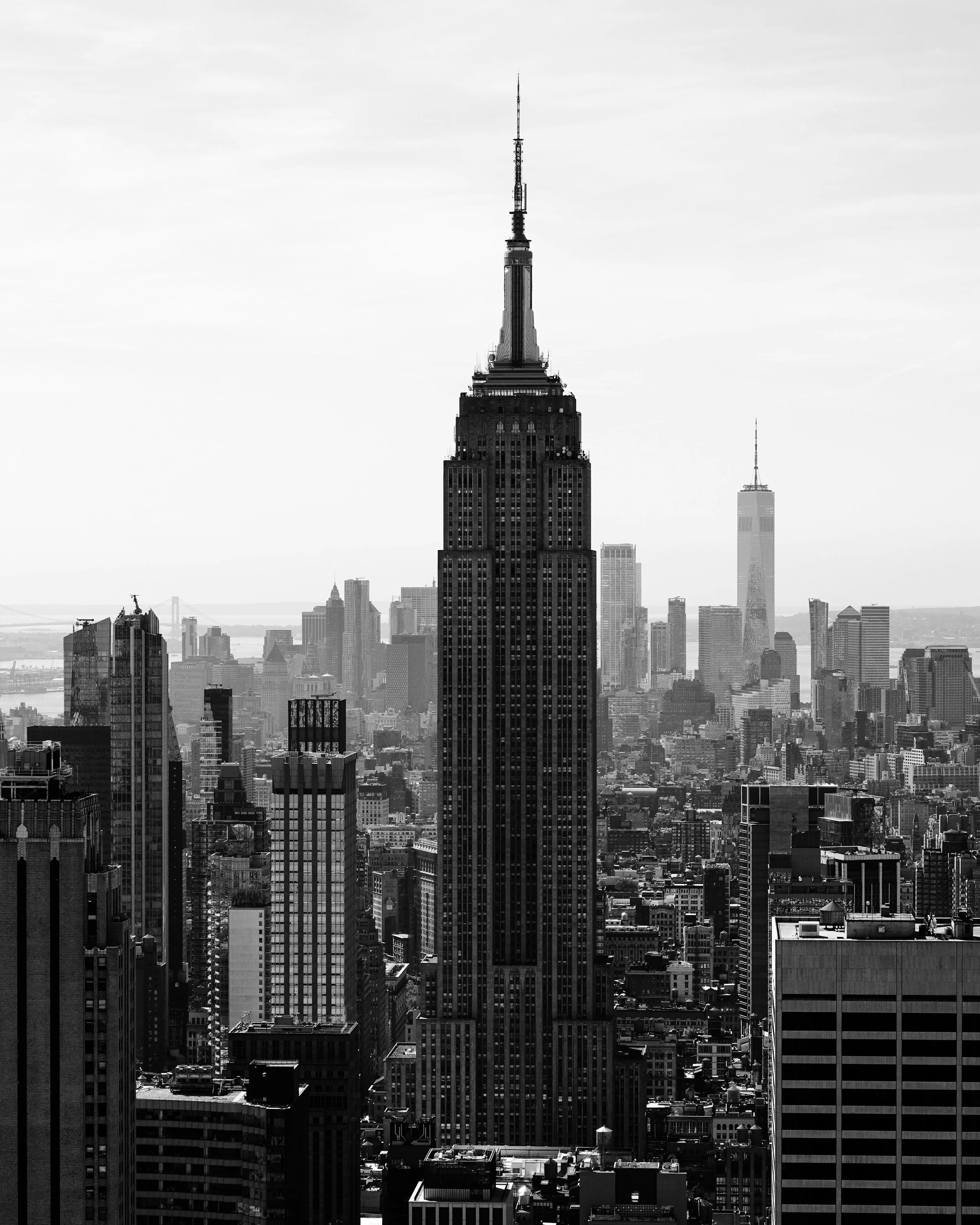 Black and white photograph of New York City skyline featuring the Empire State Building in the foreground and One World Trade Center in the background, with a view of surrounding skyscrapers and cityscape.