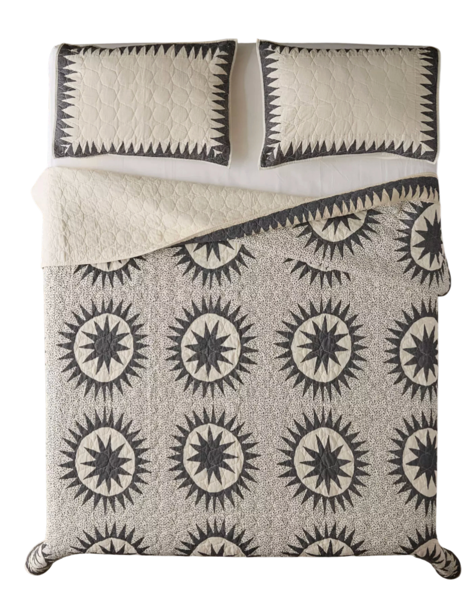 A bed with black and white starburst patterned bedspread and two matching pillows.