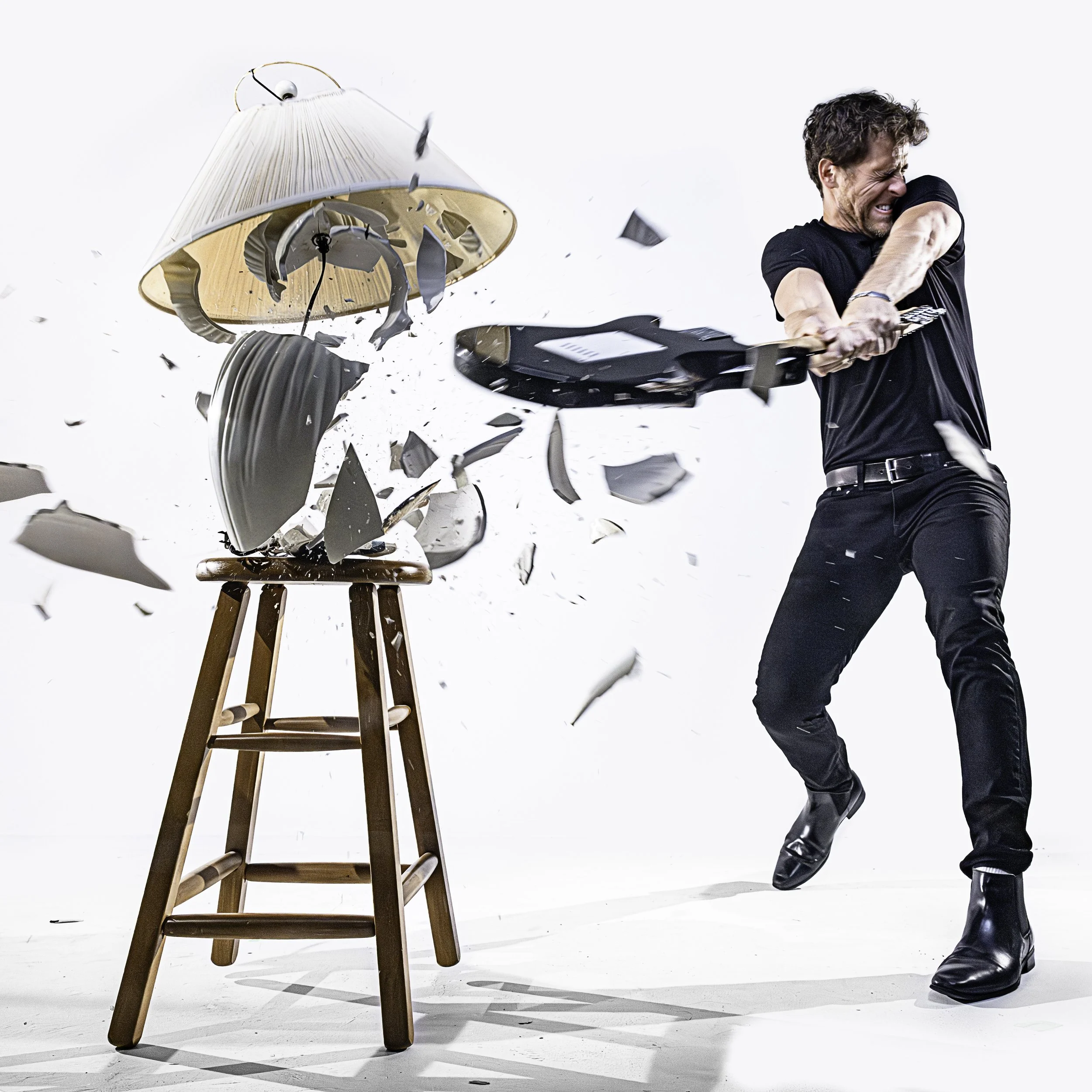 Brett Benowitz smashing a ceramic lamp with an electric guitar in a dramatic high-speed photo shoot, mid-impact, on a white backdrop.