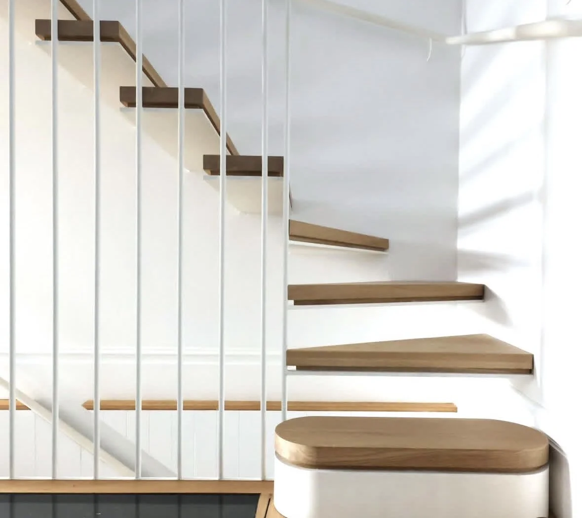 Close-up of a modern wooden staircase with white metal railing on the Left side, against a white wall, with sunlight casting shadows - Wanaka.