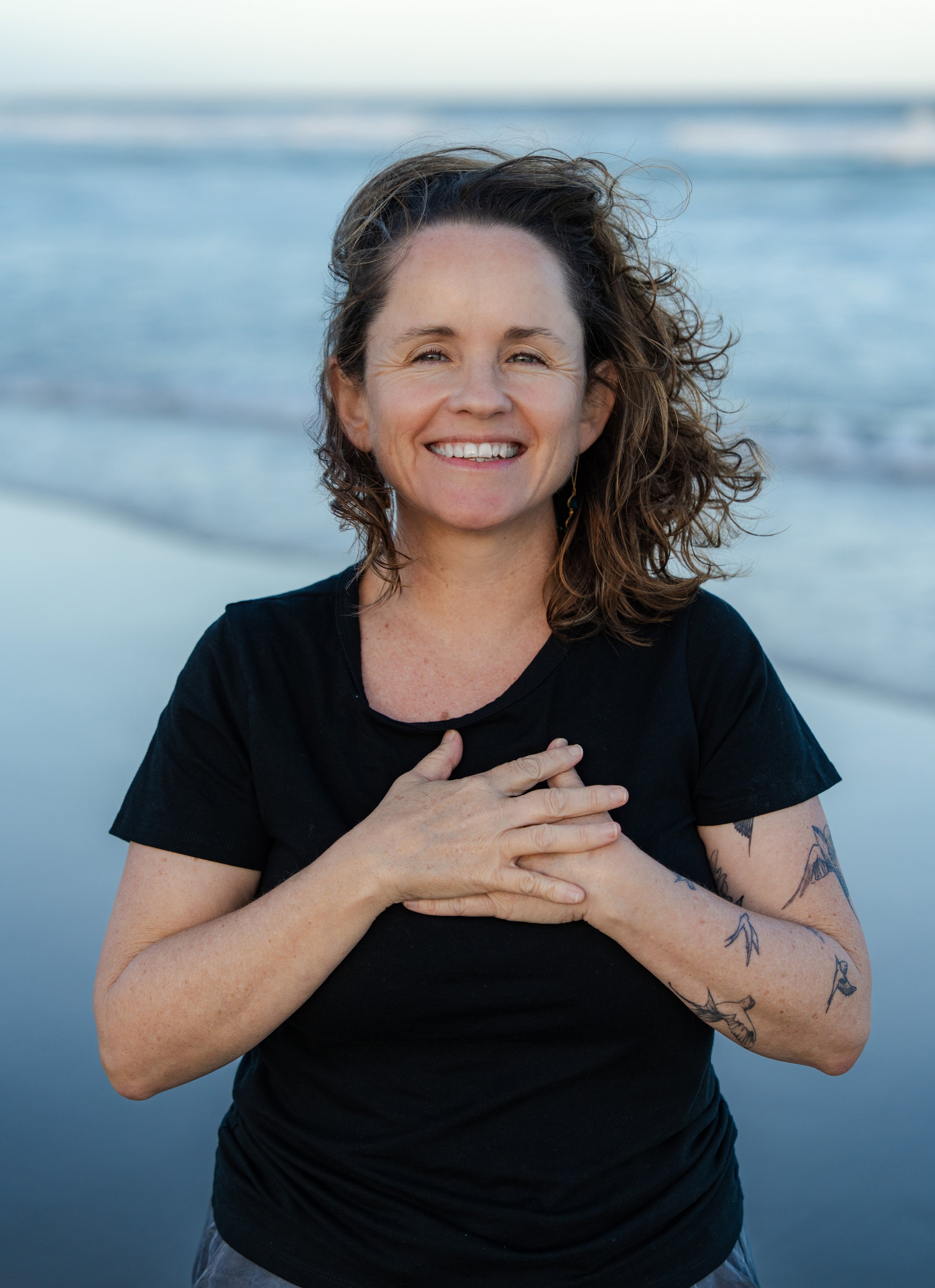Fiona on a beach with hands on heart in resourcing posture, regulating the nervous system