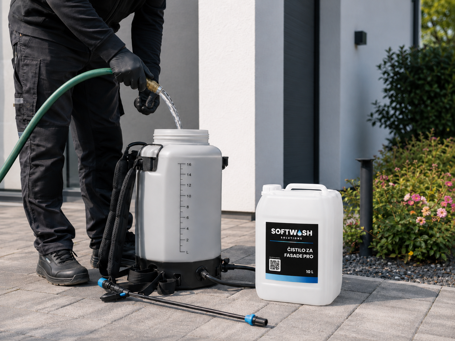 A person wearing black gloves and clothing is filling a professional spray tank with cleaning solution from a large white container labeled Softwash Solutions, outside a modern building with plants nearby.