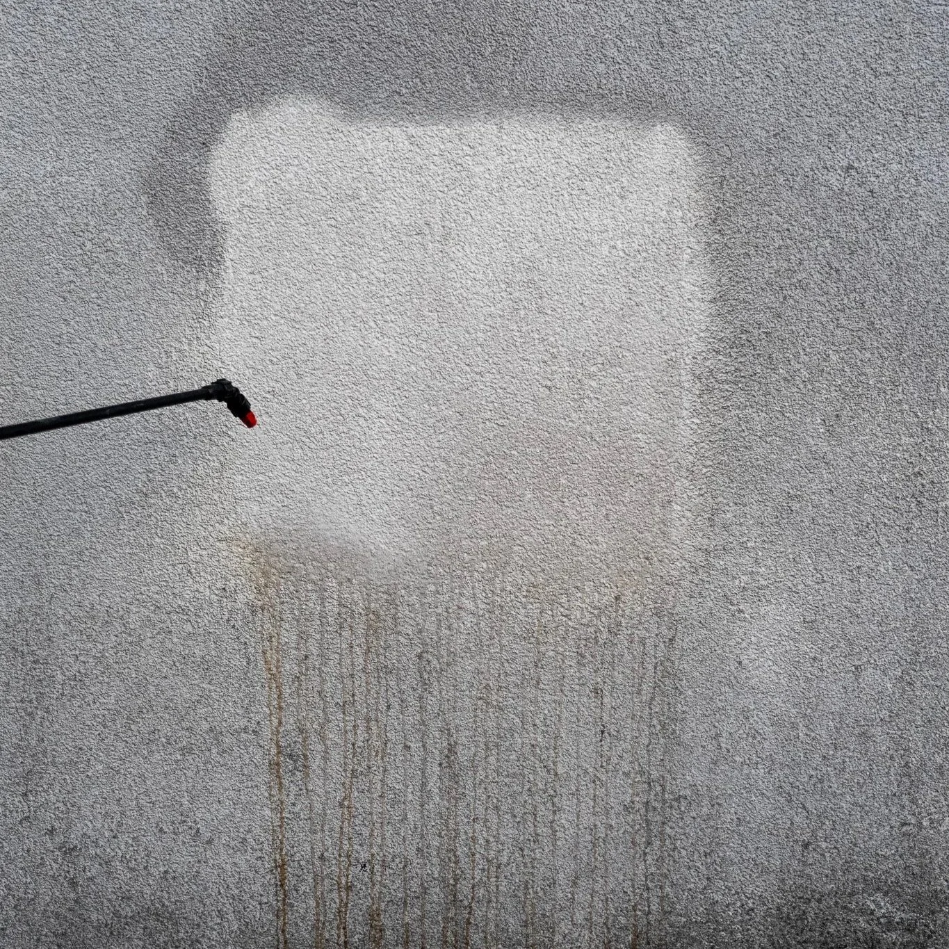 A pressure washer spraying water onto a textured wall, removing dirt and stains.