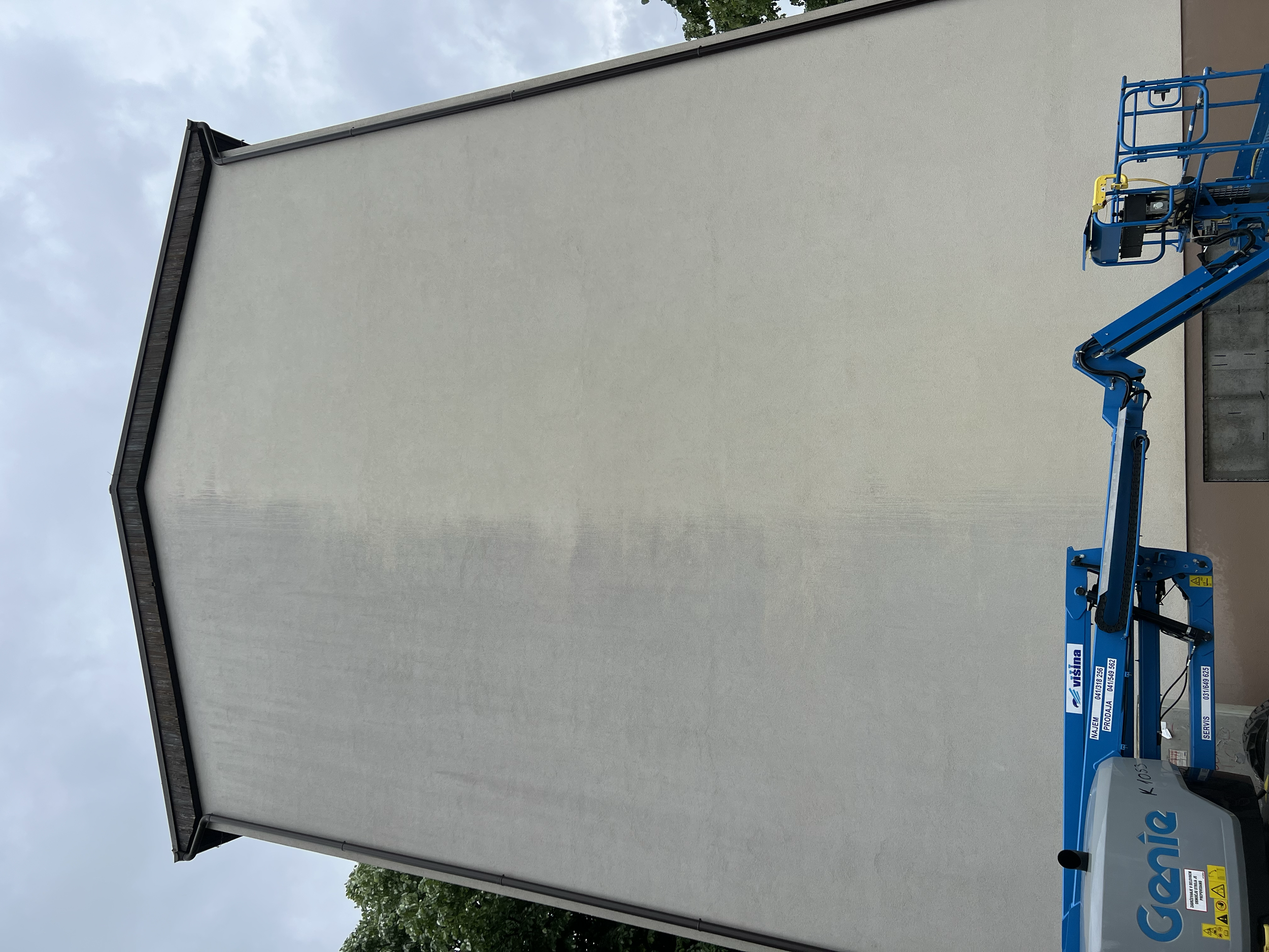 A large, plain white projection screen or backdrop on a blue scissor lift or boom lift outside against an overcast sky.