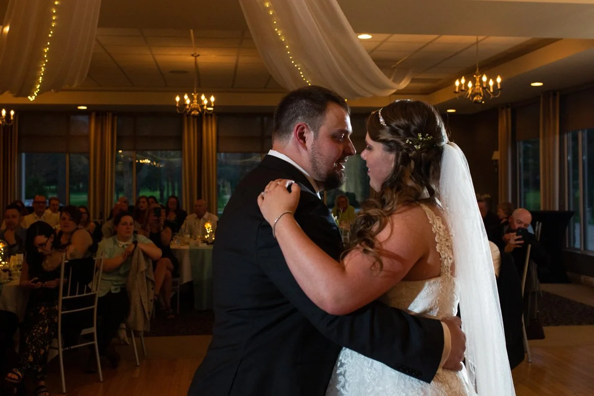A bride and groom dance closely during their wedding reception, with guests watching and taking photos in the background.