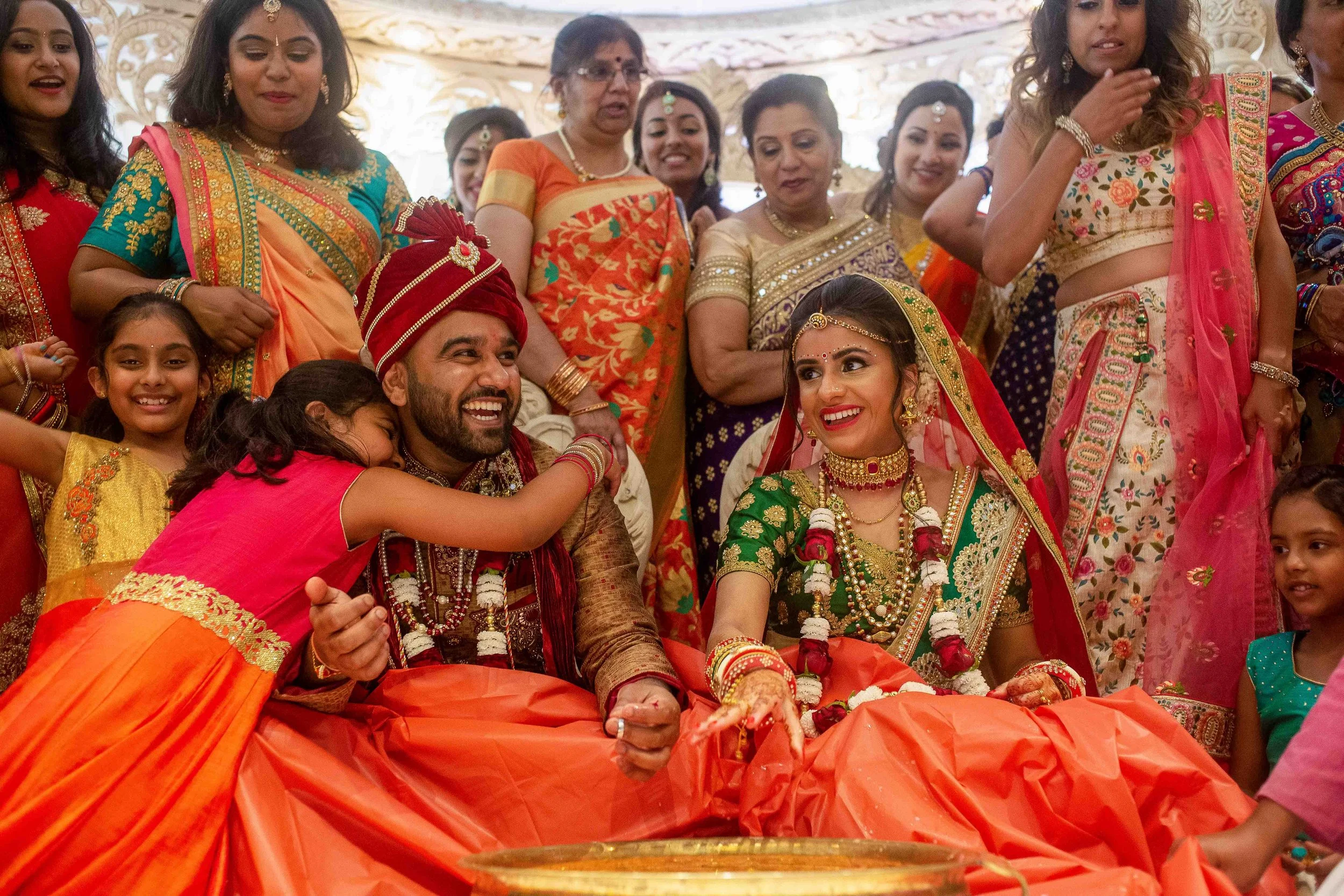 Indian wedding ceremony with bride and groom surrounded by family and friends, wearing colorful traditional attire.