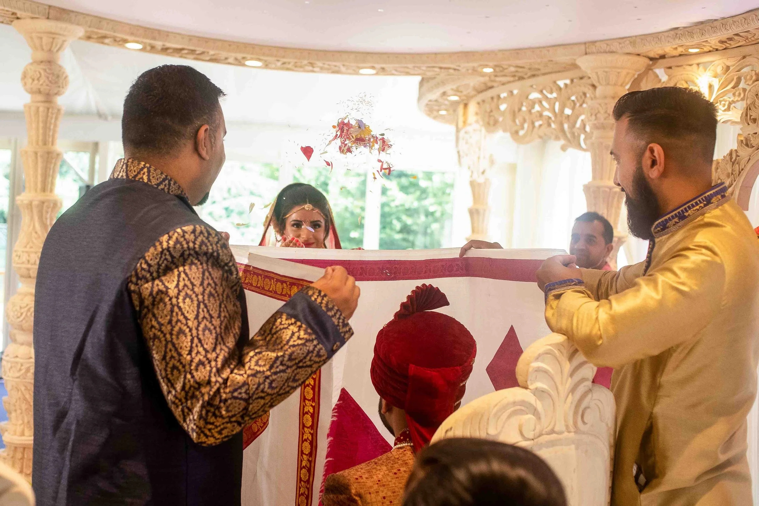 Indian wedding ceremony with the bride and groom exchanging vows beneath a decorated canopy, surrounded by family and friends in traditional attire.