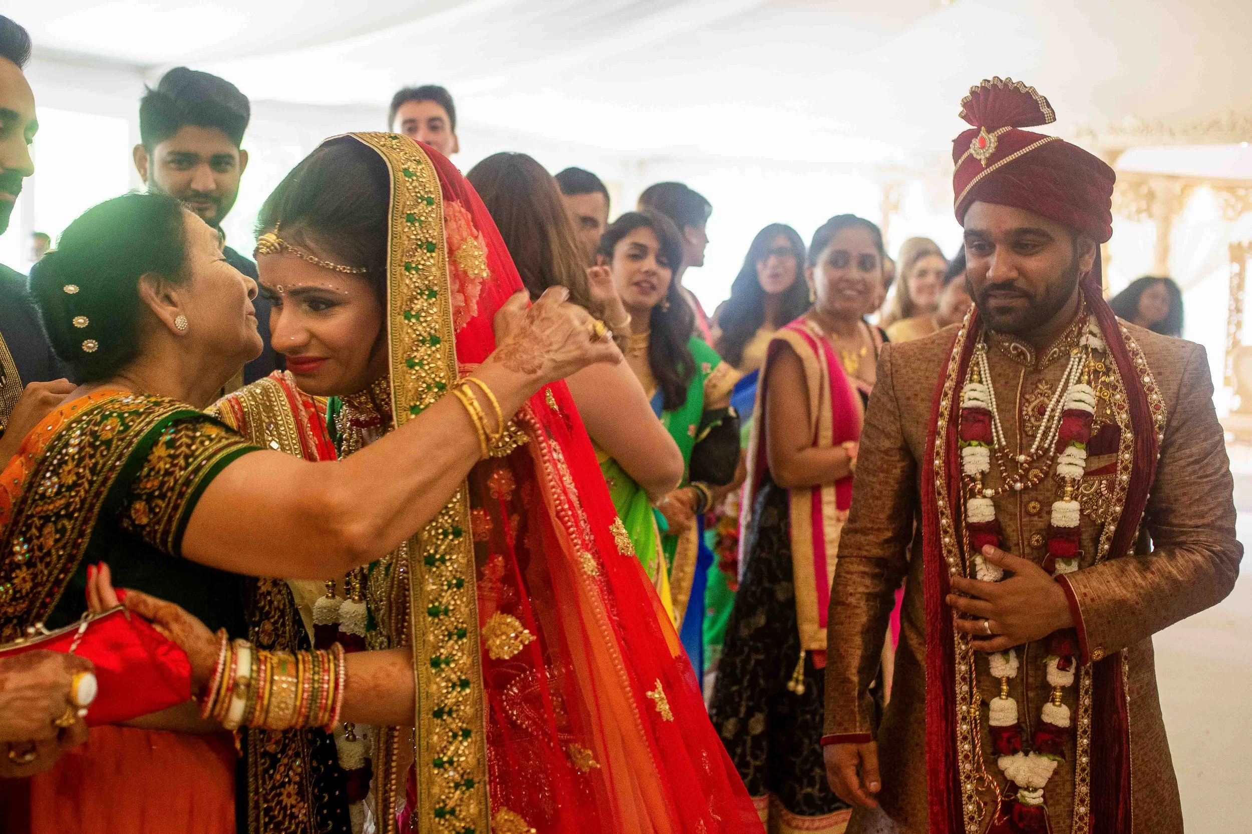 Indian wedding ceremony with bride and groom dressed in traditional wedding attire, surrounded by family and friends in colorful sarees and sherwanis, inside a decorated venue.