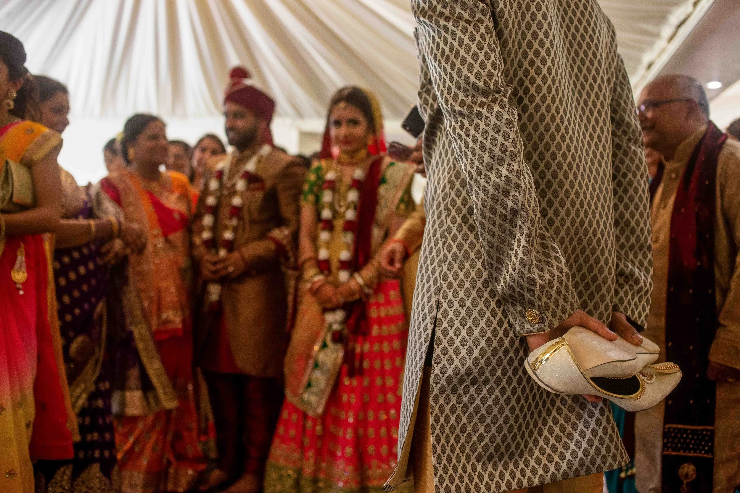 People dressed in traditional Indian attire at a wedding or celebration, gathered inside a decorated tent.