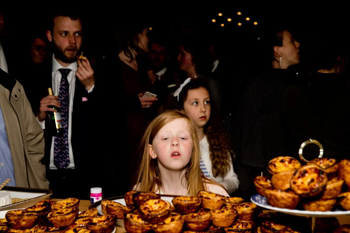 Young girls looking at a table of muffins at a crowded event with people in the background.