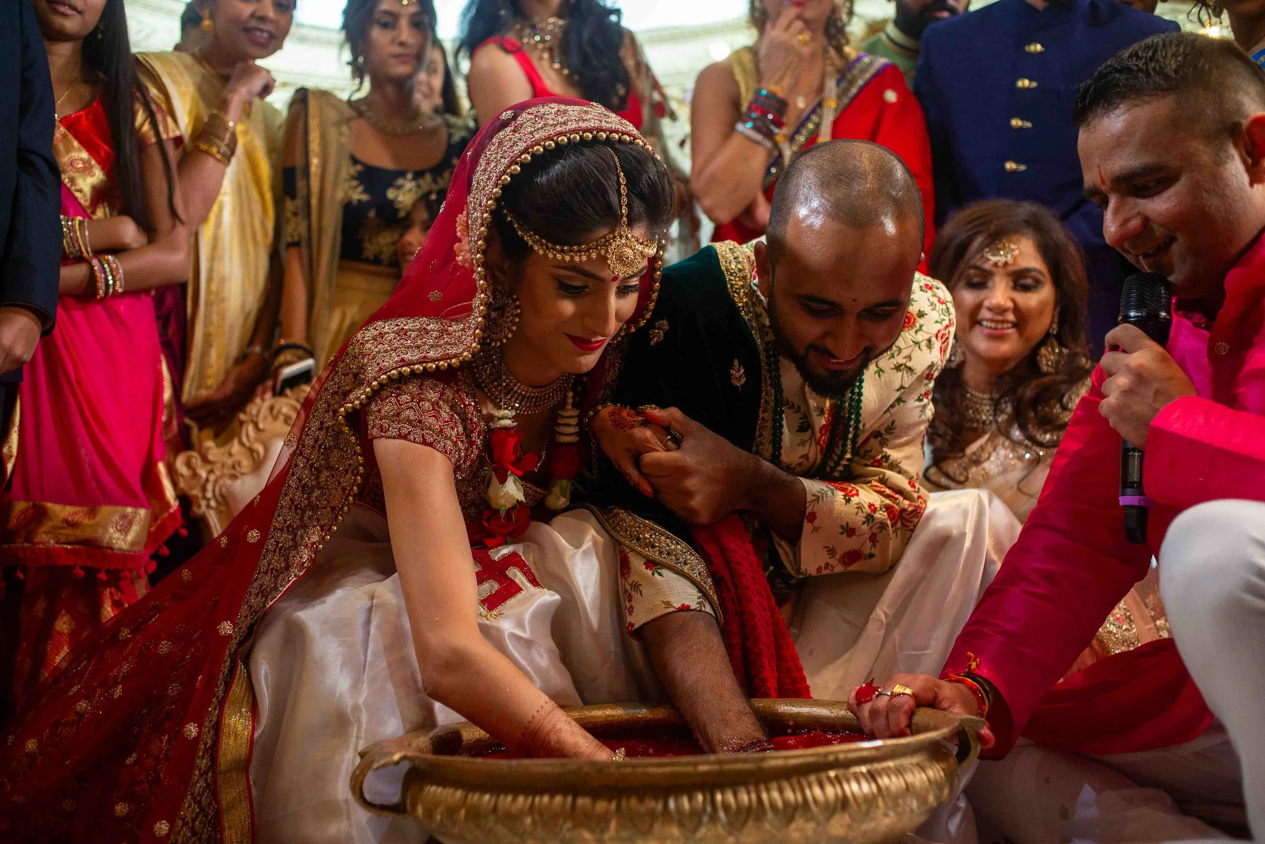 Indian wedding ceremony with bride and groom participating in a traditional ritual, surrounded by family and friends in festive attire.