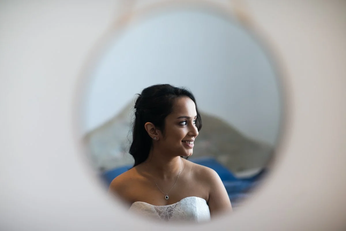 A woman smiling, seen through a circular mirror, with a mountain landscape in the background.