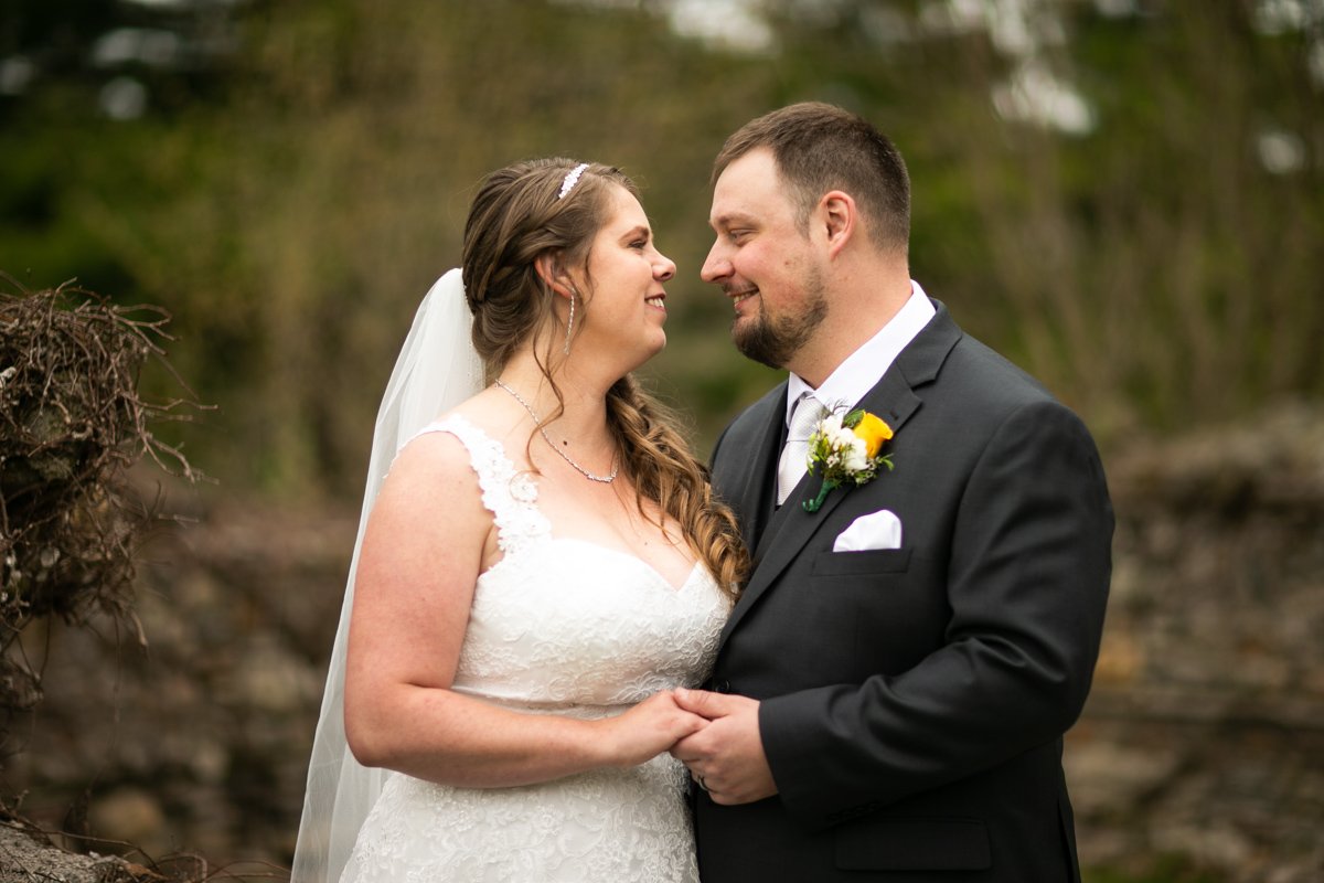 A bride and groom smiling at each other outdoors on their wedding day.