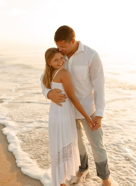 Couple embracing on a beach with waves in the background during sunset.