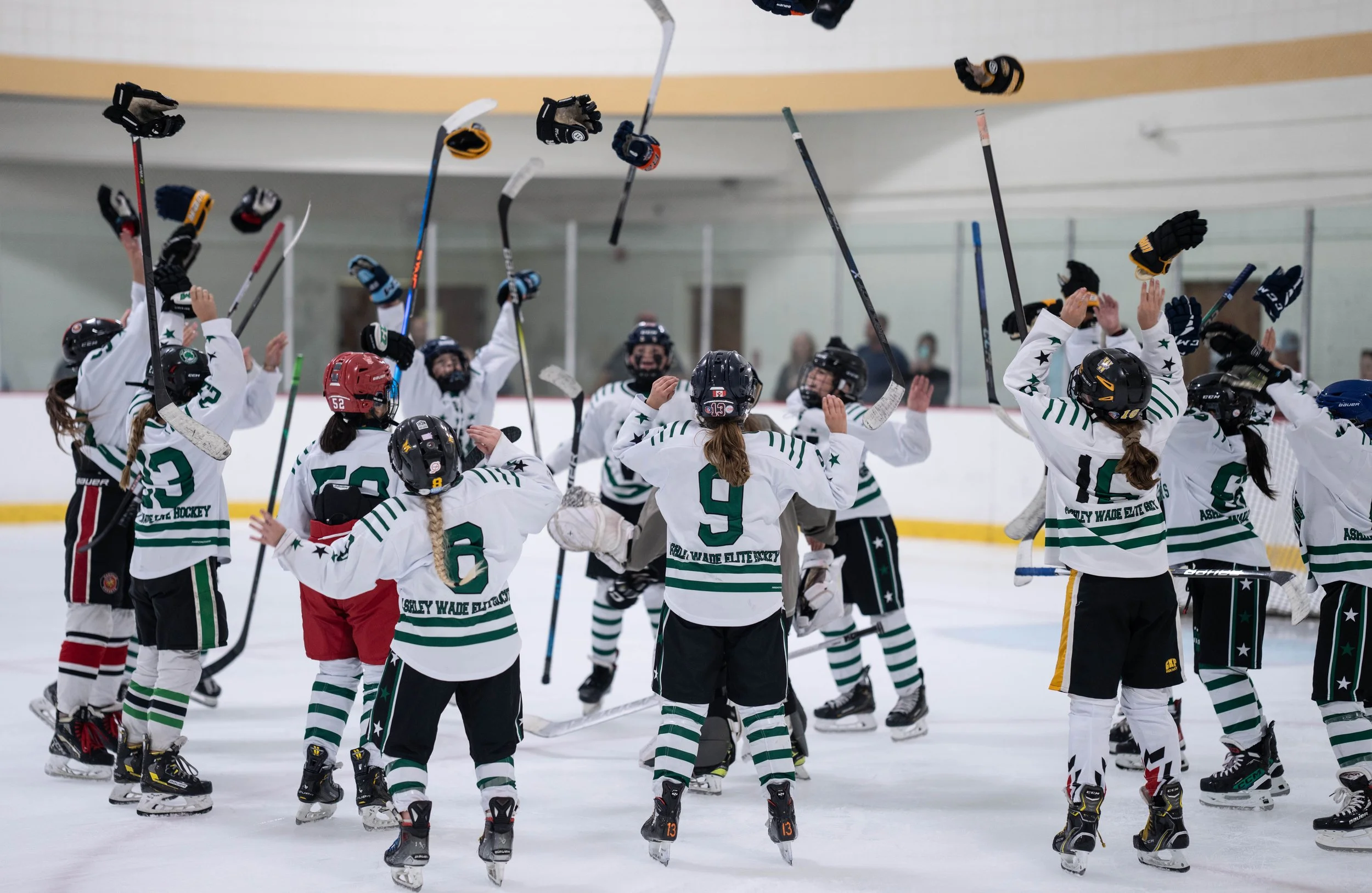 Youth hockey team celebrating on ice, throwing helmets and gloves in air.