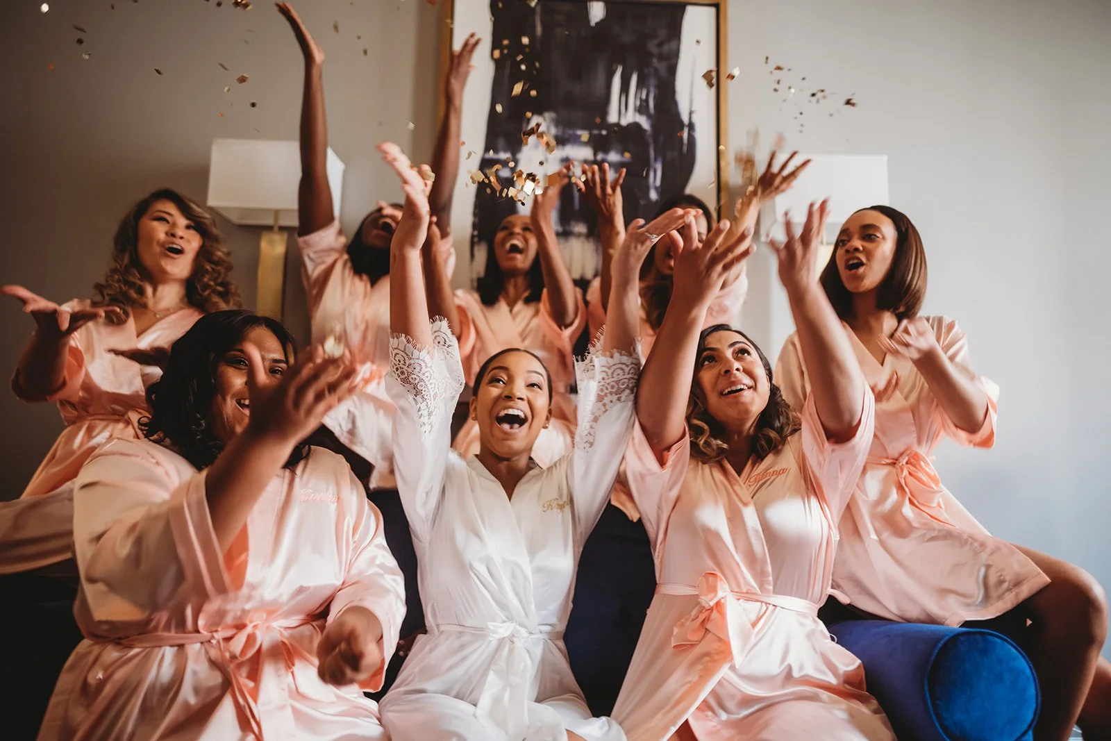 Group of women in matching robes celebrating and throwing confetti indoors.