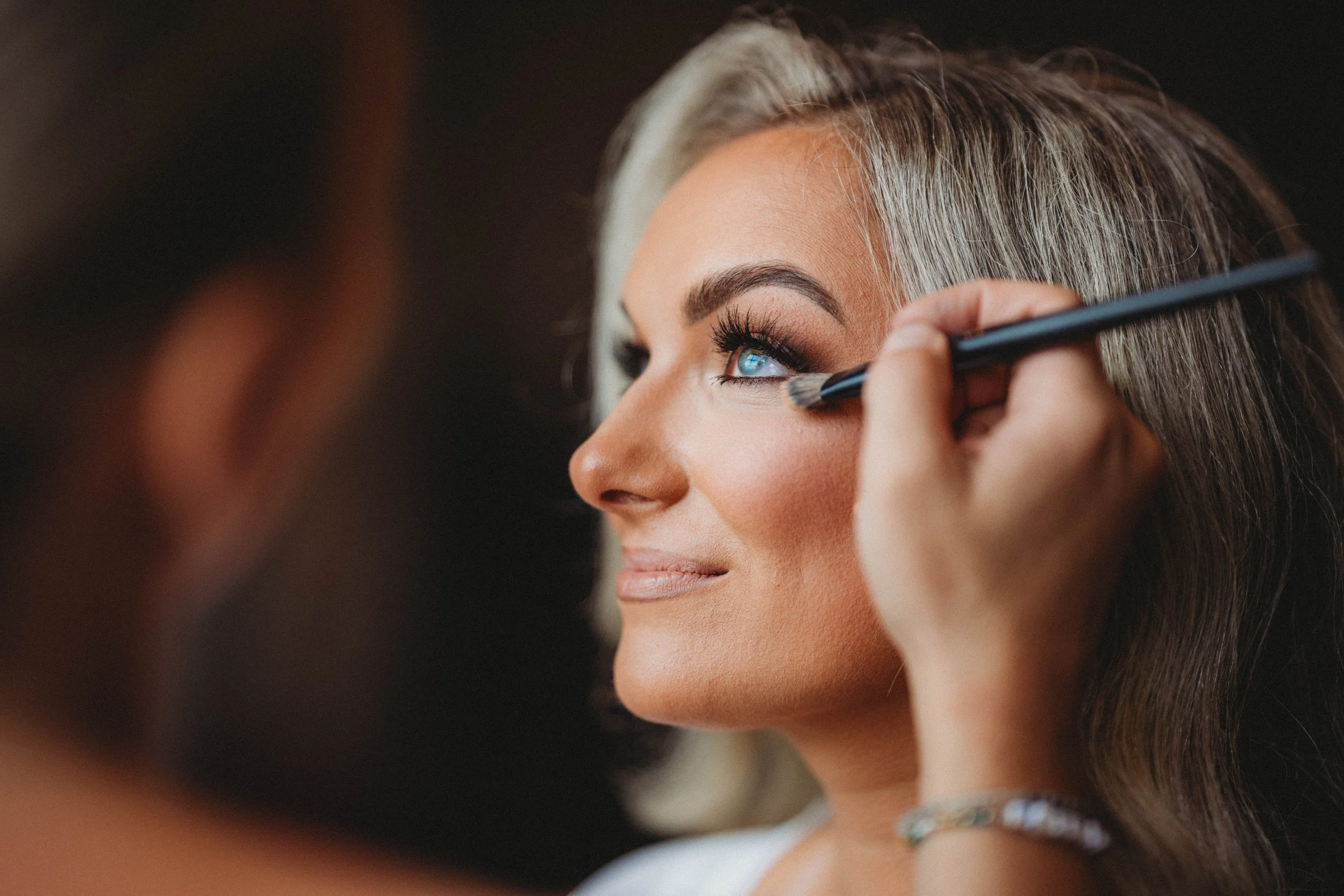 Close-up of a woman having makeup applied with a brush, focusing on her eyes and cheeks.