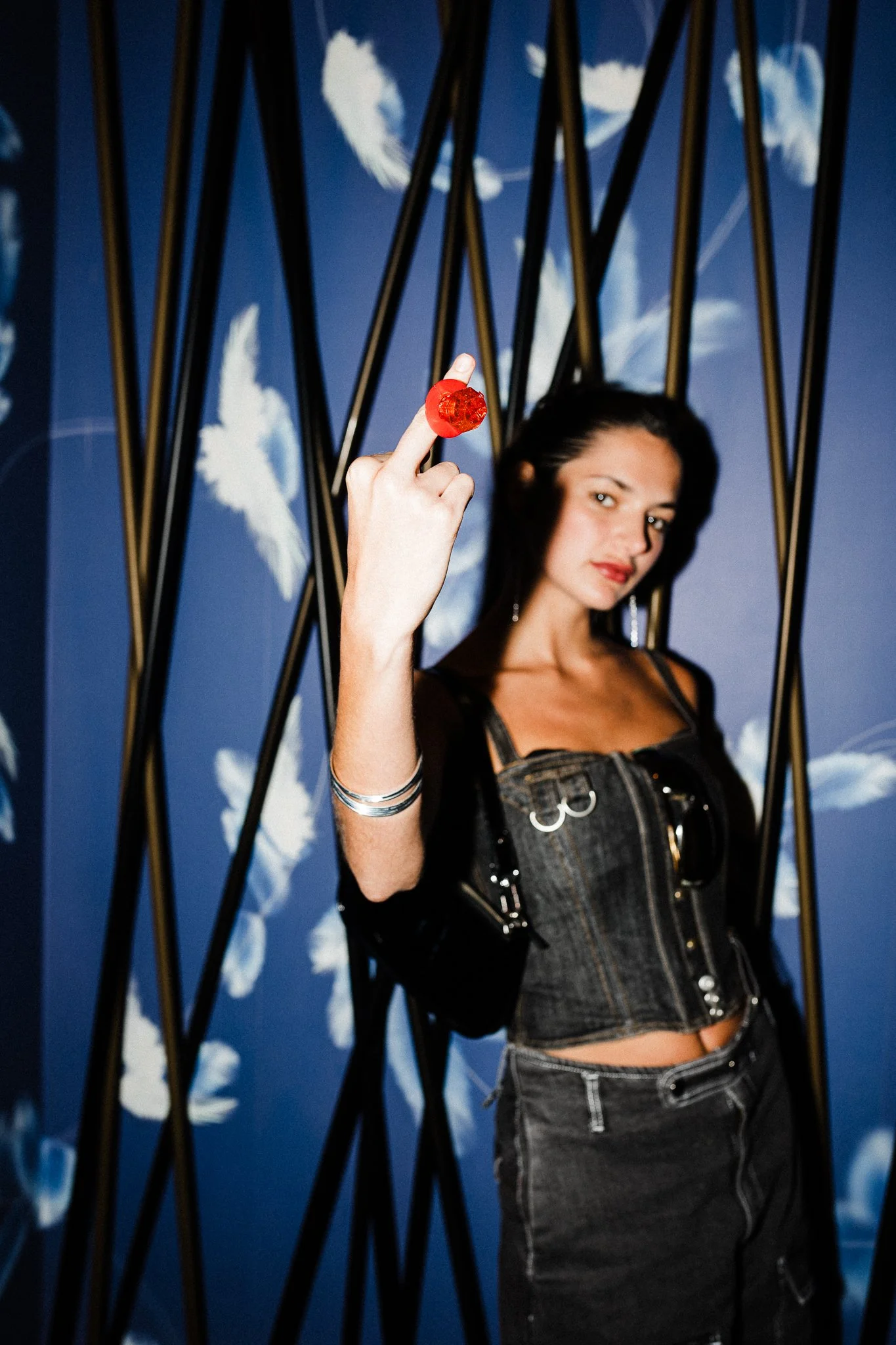 Woman in denim outfit holding a red lollipop in front of a blue floral background.