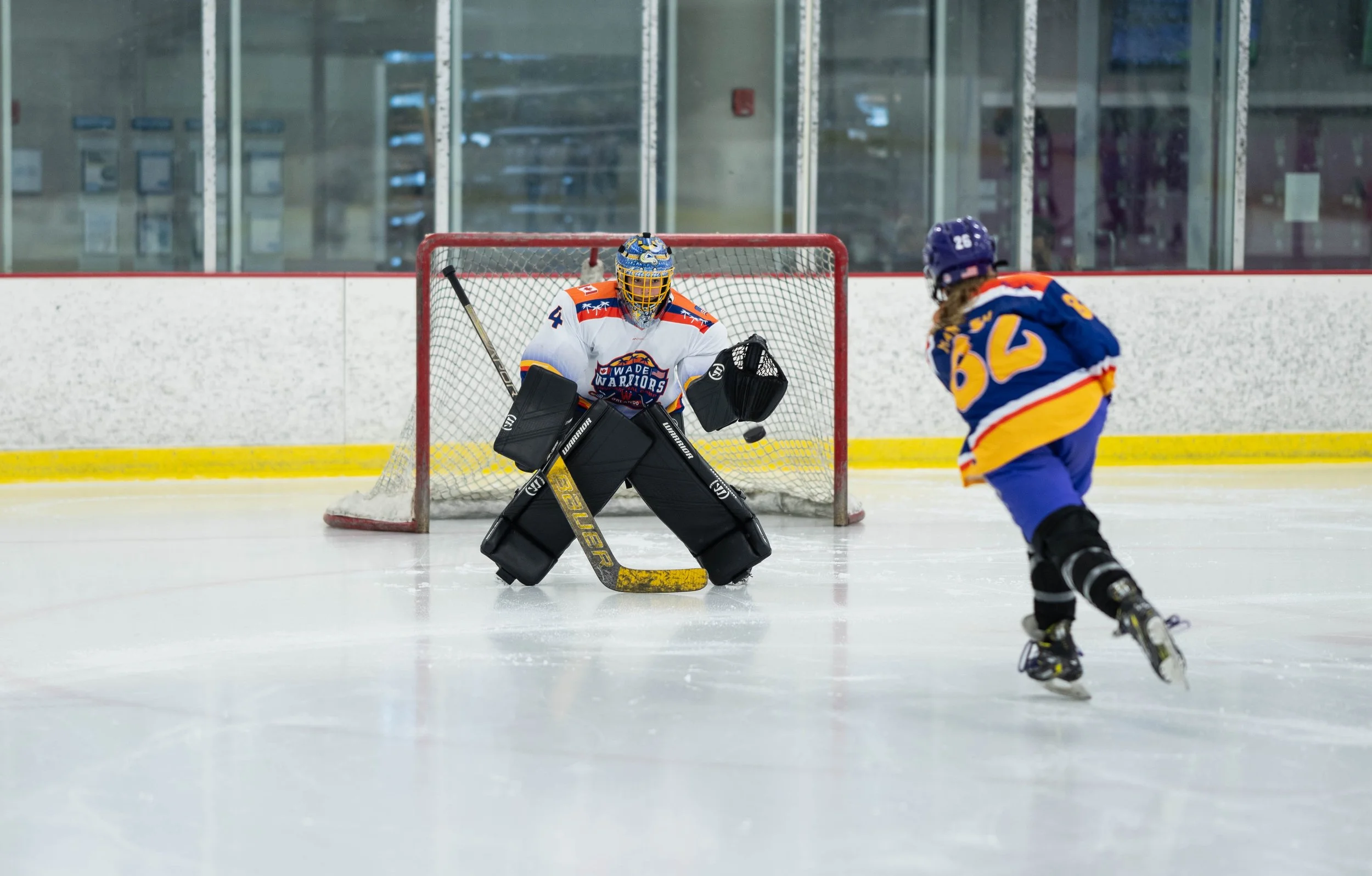 Ice hockey player shooting at goalie in front of goal net