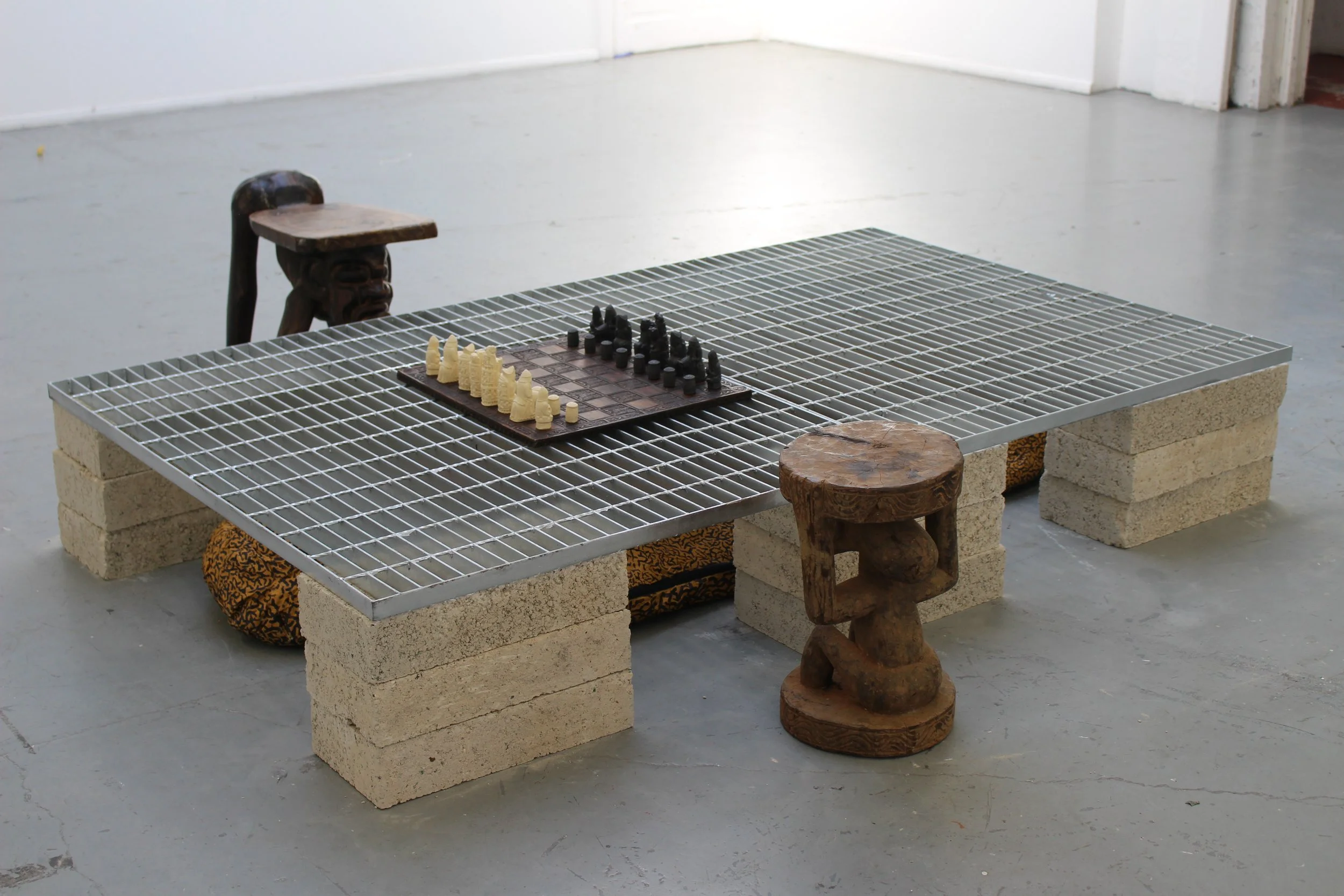 One Eye Shut, 2024. Installation. Metal grille, acrylic paint on sleeping bag, cinder blocks, chess game, wooden stools — 200 x 120 cm. 