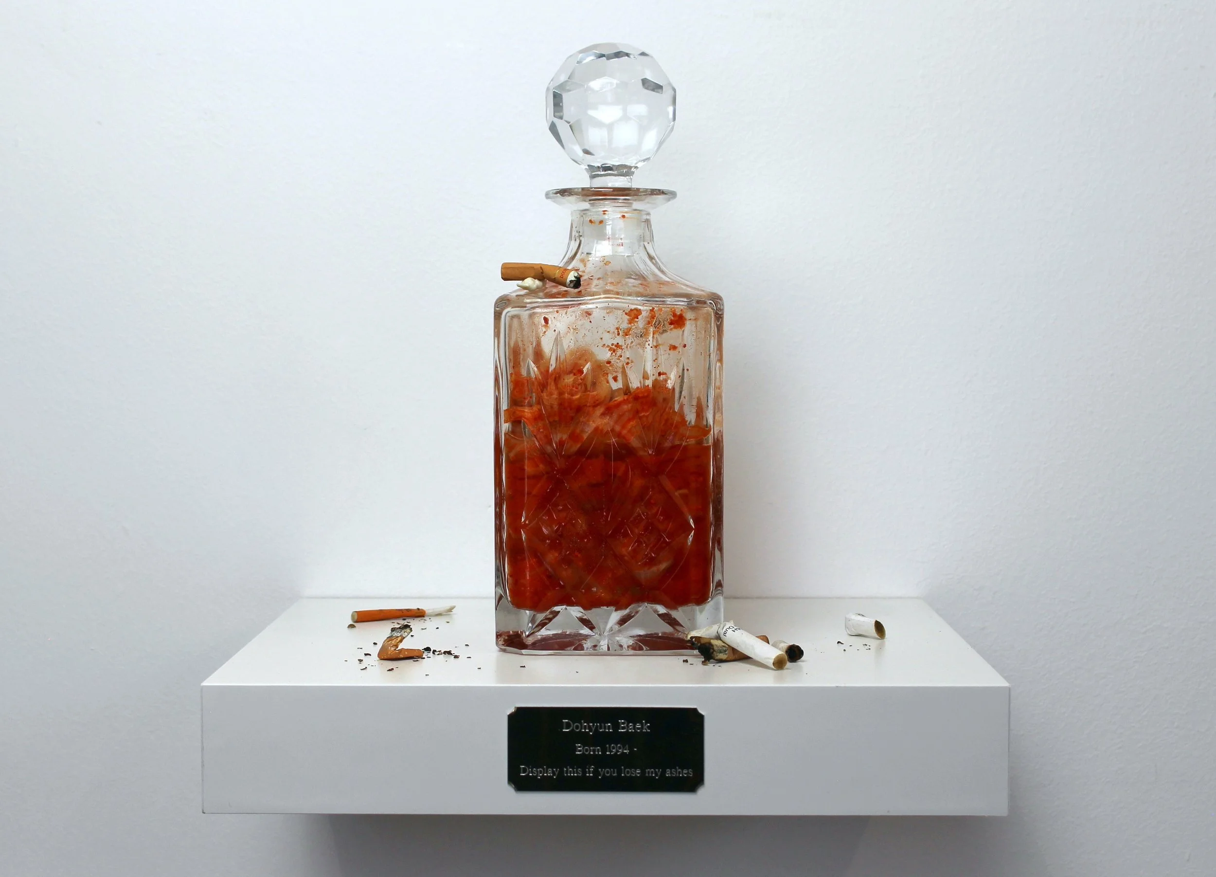 Display This If You Lose My Ashes, 2024. Kimchi, whiskey decanter, chewing gum, cigarettes, metal plate — 30 x 30 x 26 cm