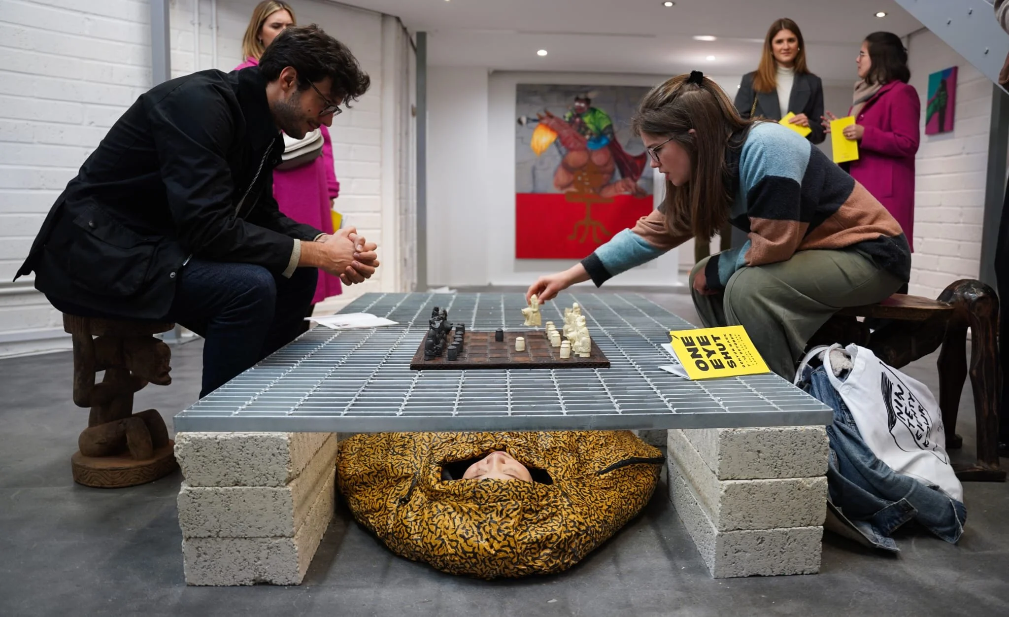 One Eye Shut, 2024. Installation and participatory performance. Metal grille, acrylic paint on sleeping bag, cinder blocks, chess game, wooden stools — 200 x 120 cm. 