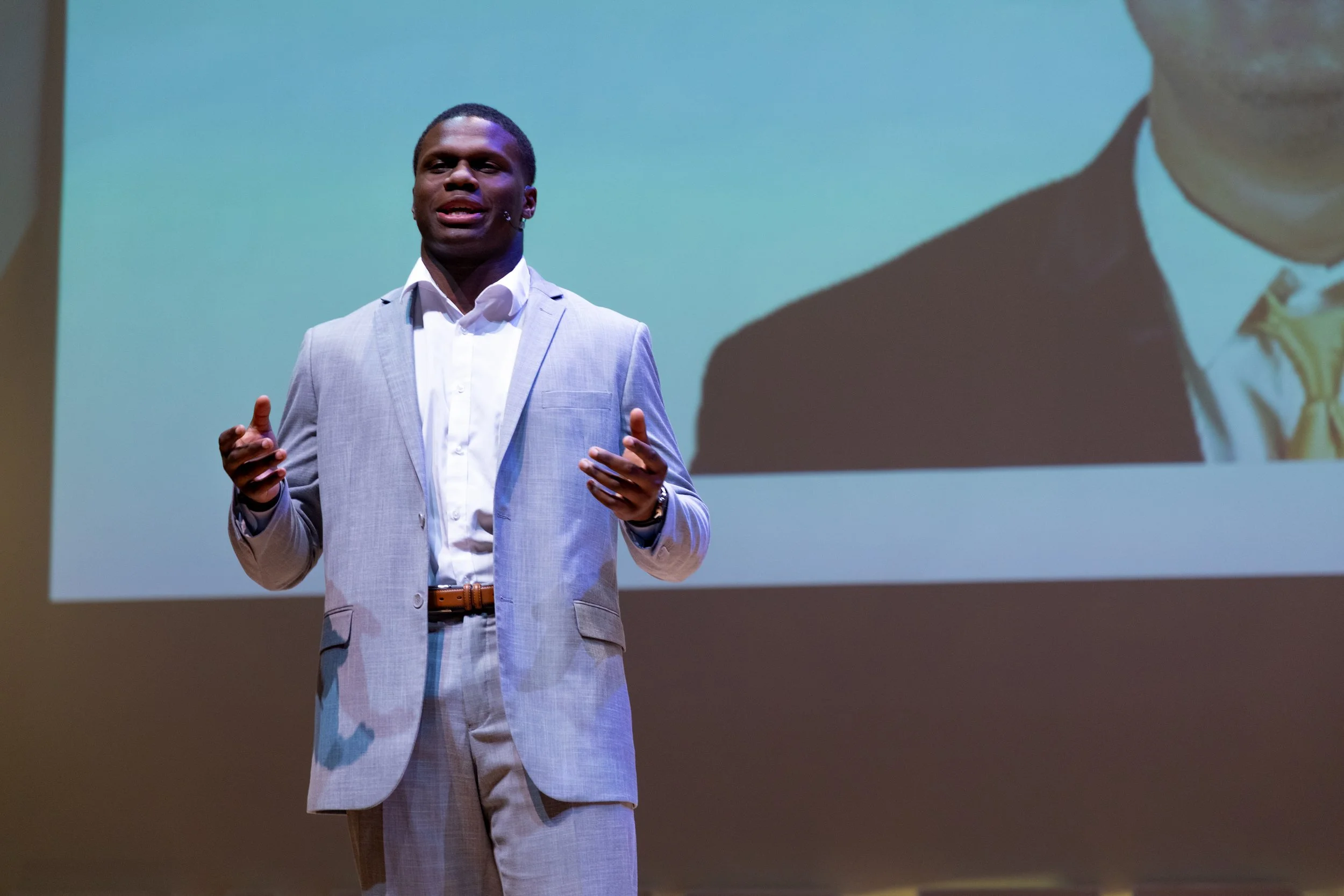 A young man in a blue suit and white shirt smiling outside a historic building with stone columns.