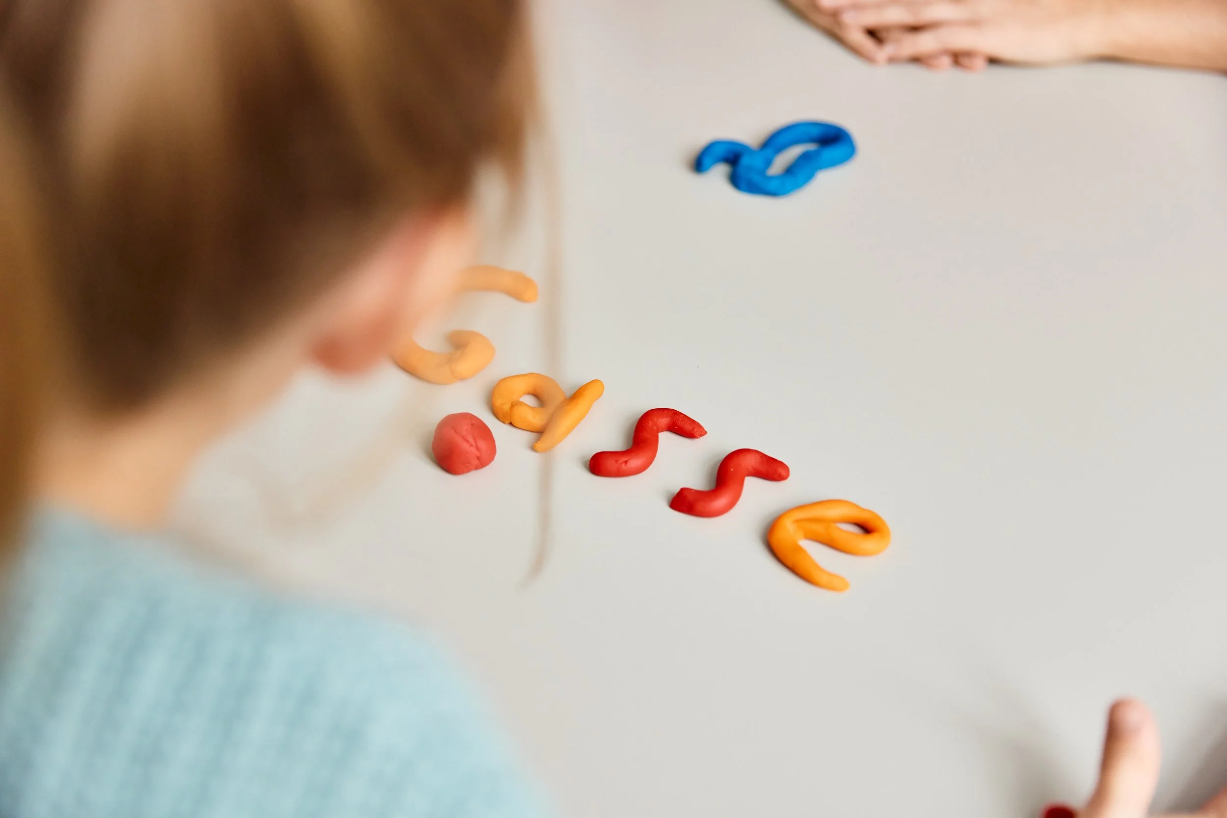 Ein Kind sieht auf bunte Knetstücke in Form von Buchstaben, die auf einem weißen Tisch liegen.