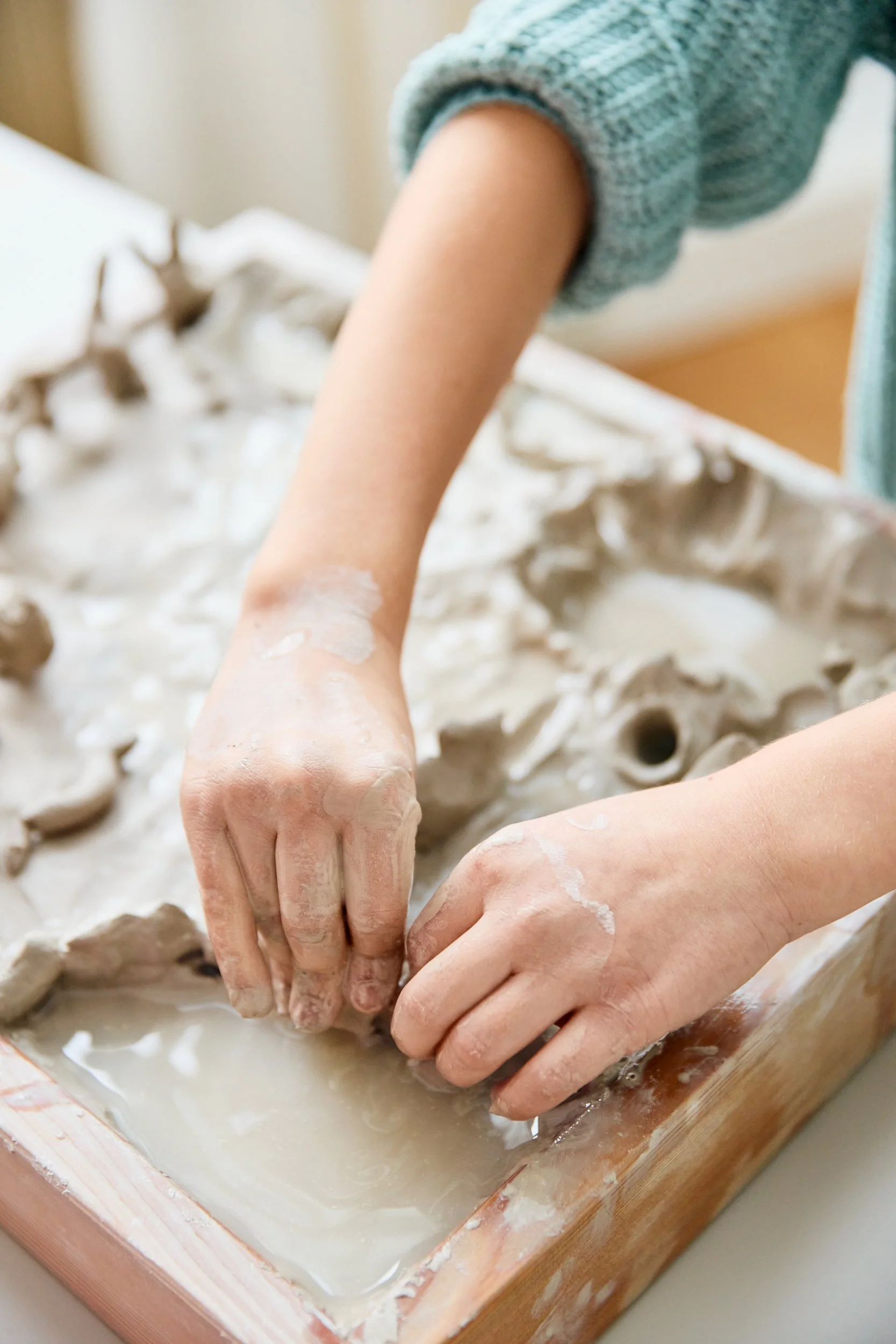 Jemand formt grau Weich ton in einer Holzwanne mit Wasser.