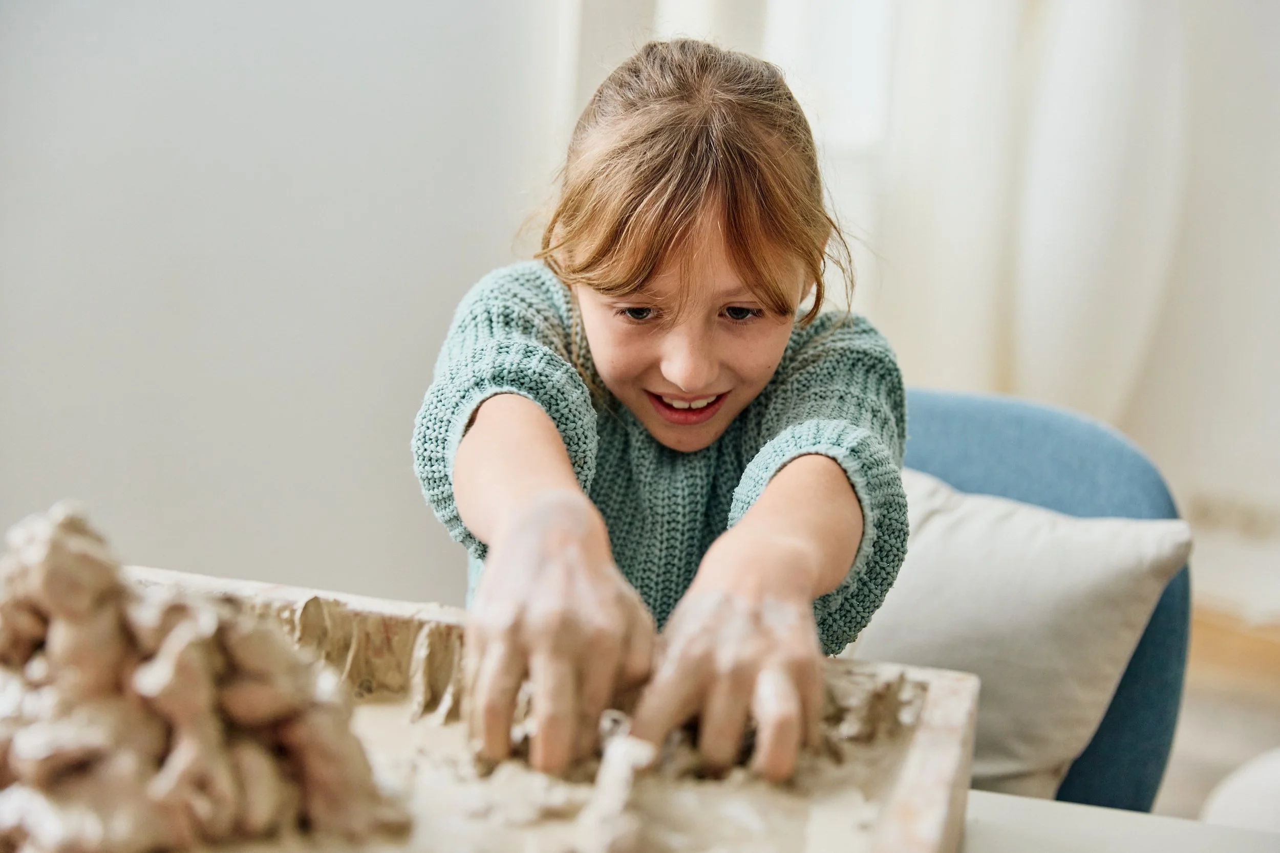 Ein Mädchen spielt begeistert mit Ton und bastelt kreativ in einem Wohnzimmer.